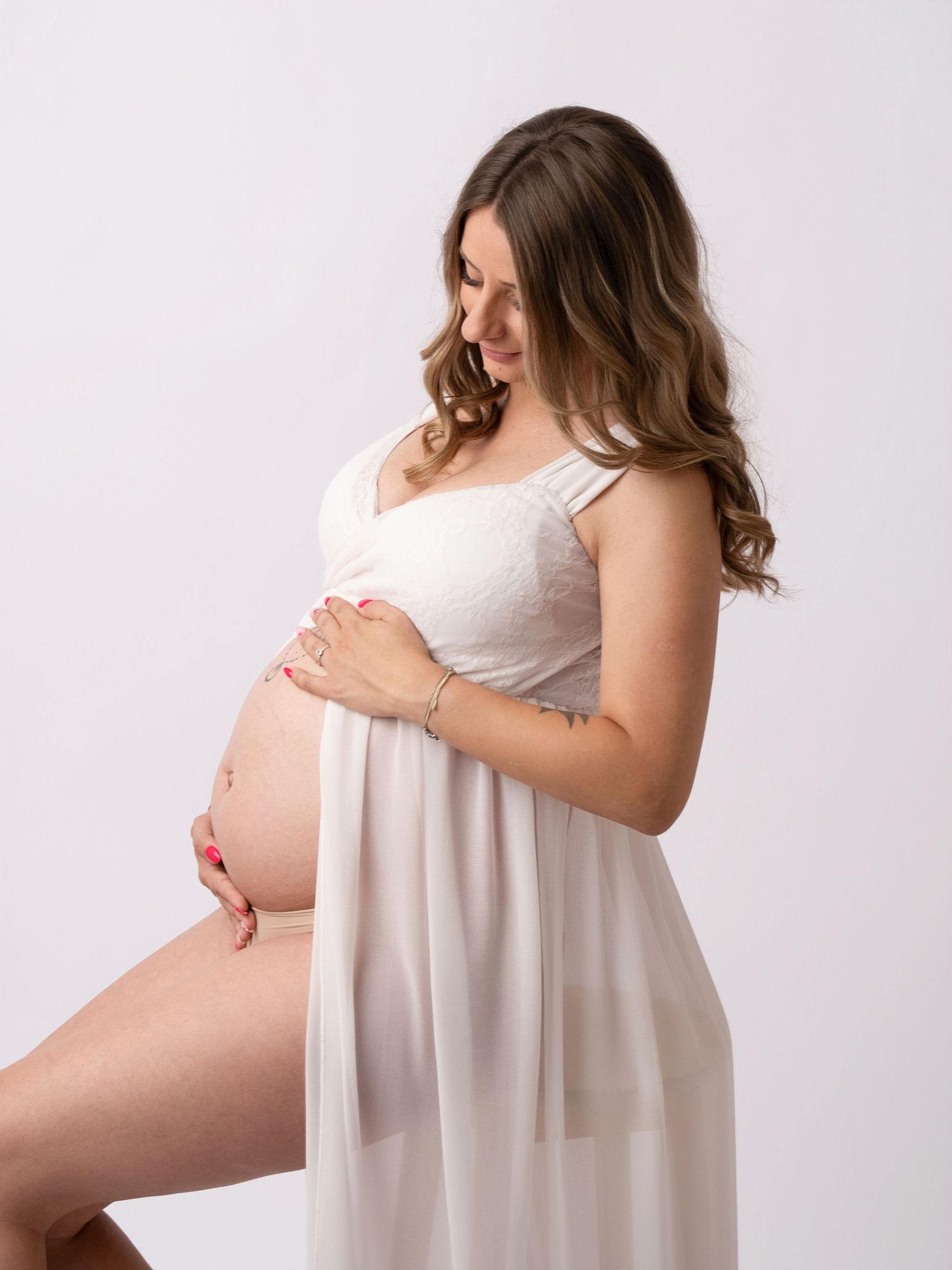 Pregnant woman in white dress cradling her baby bump during a professional maternity photo session.