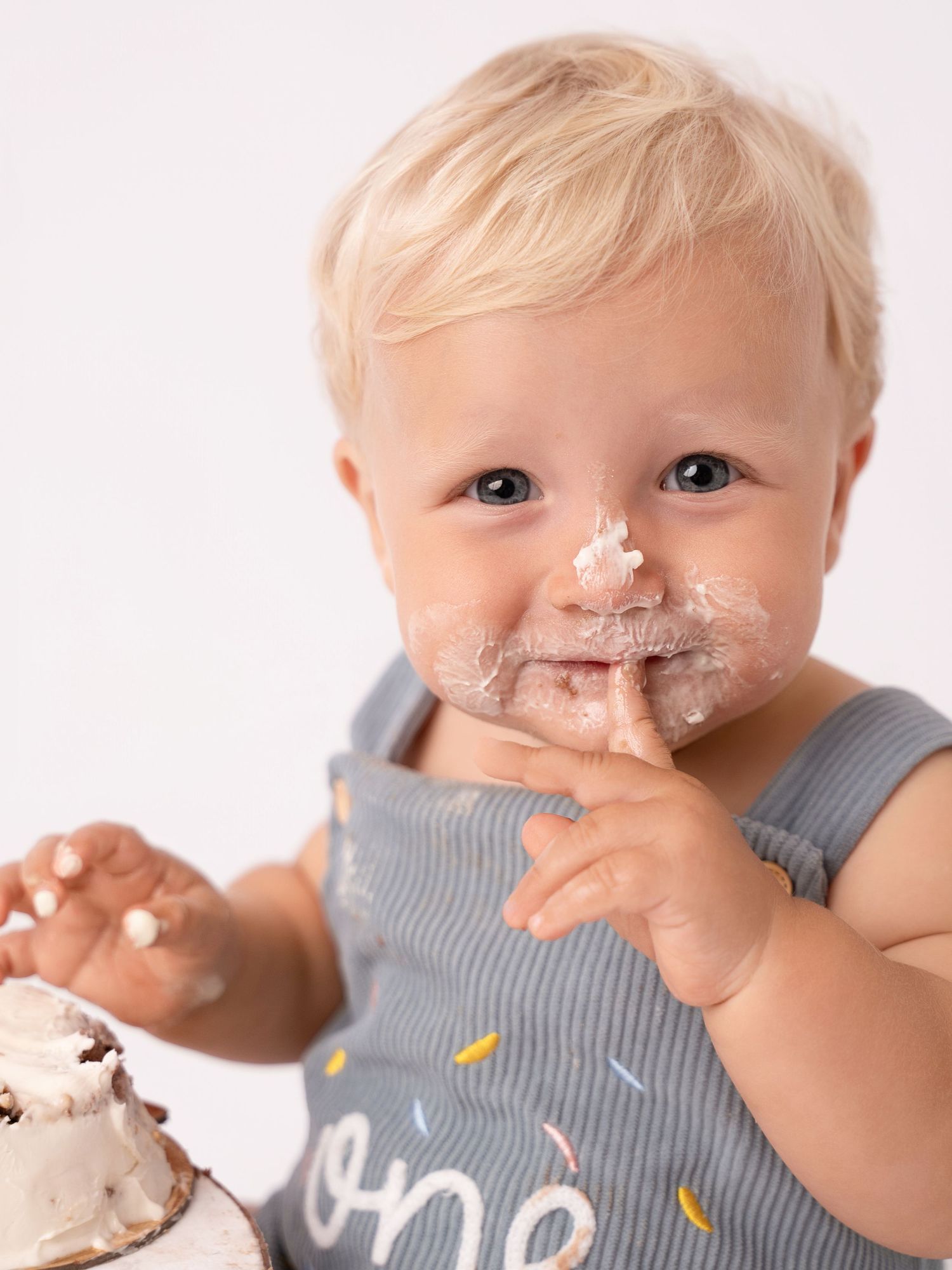 A blond toddler with cake frosting on their face wearing an 