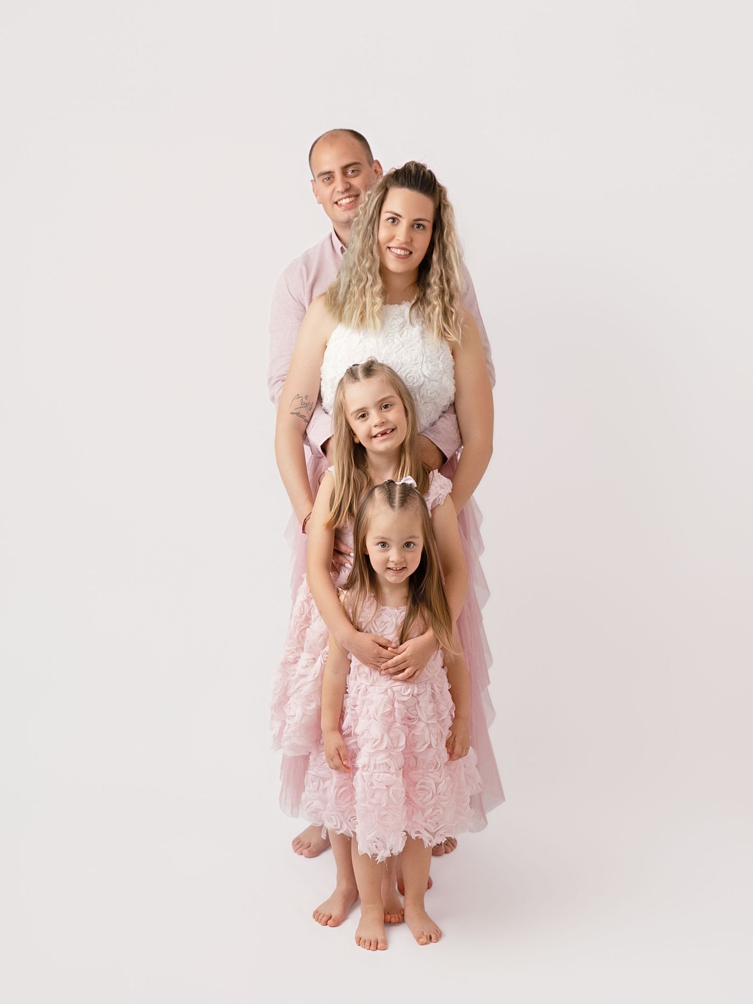 Family of four posing together in matching pink outfits against a white studio background.
