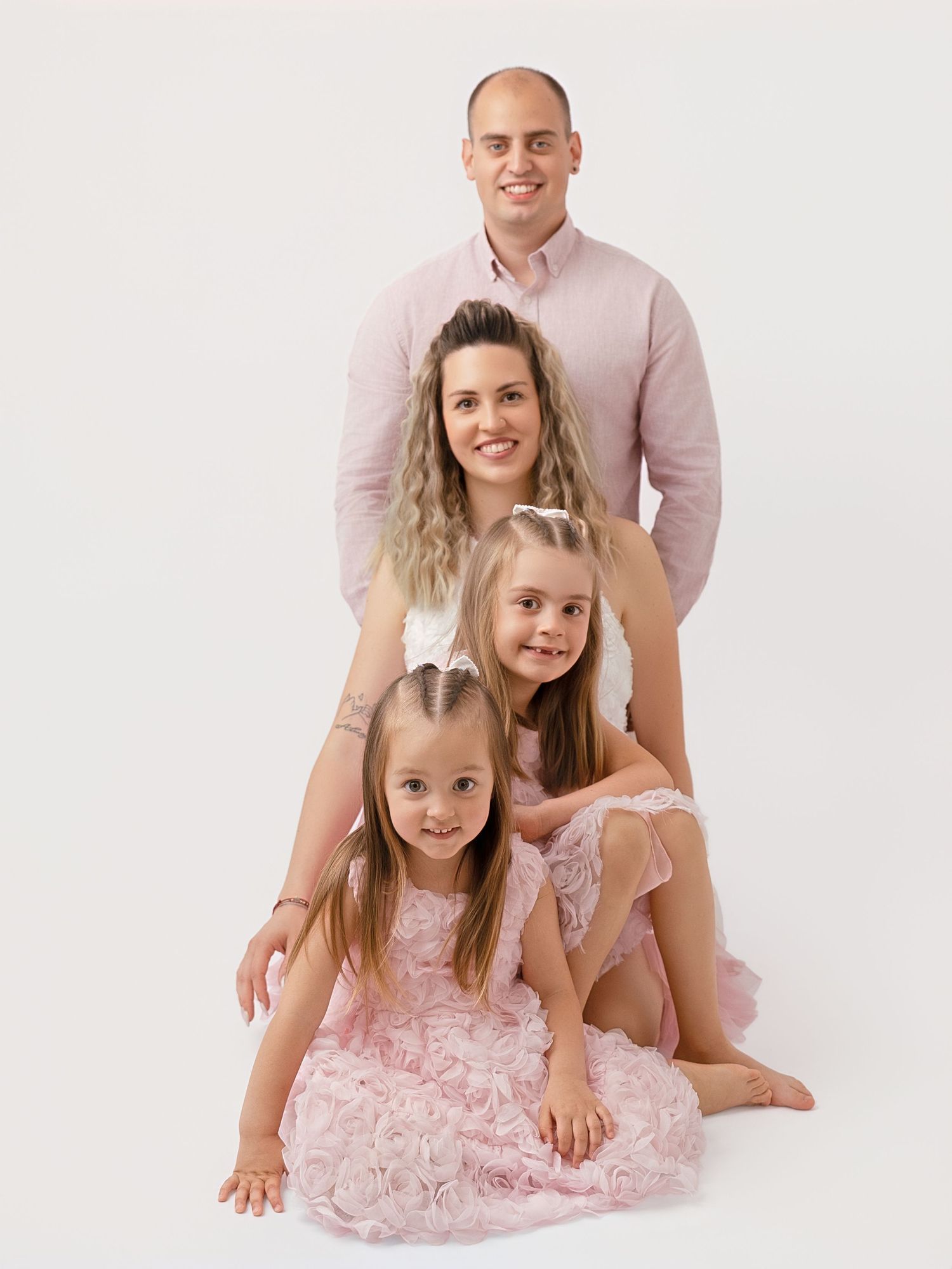 Family of four in coordinating pink outfits posing together in a bright studio portrait setting.