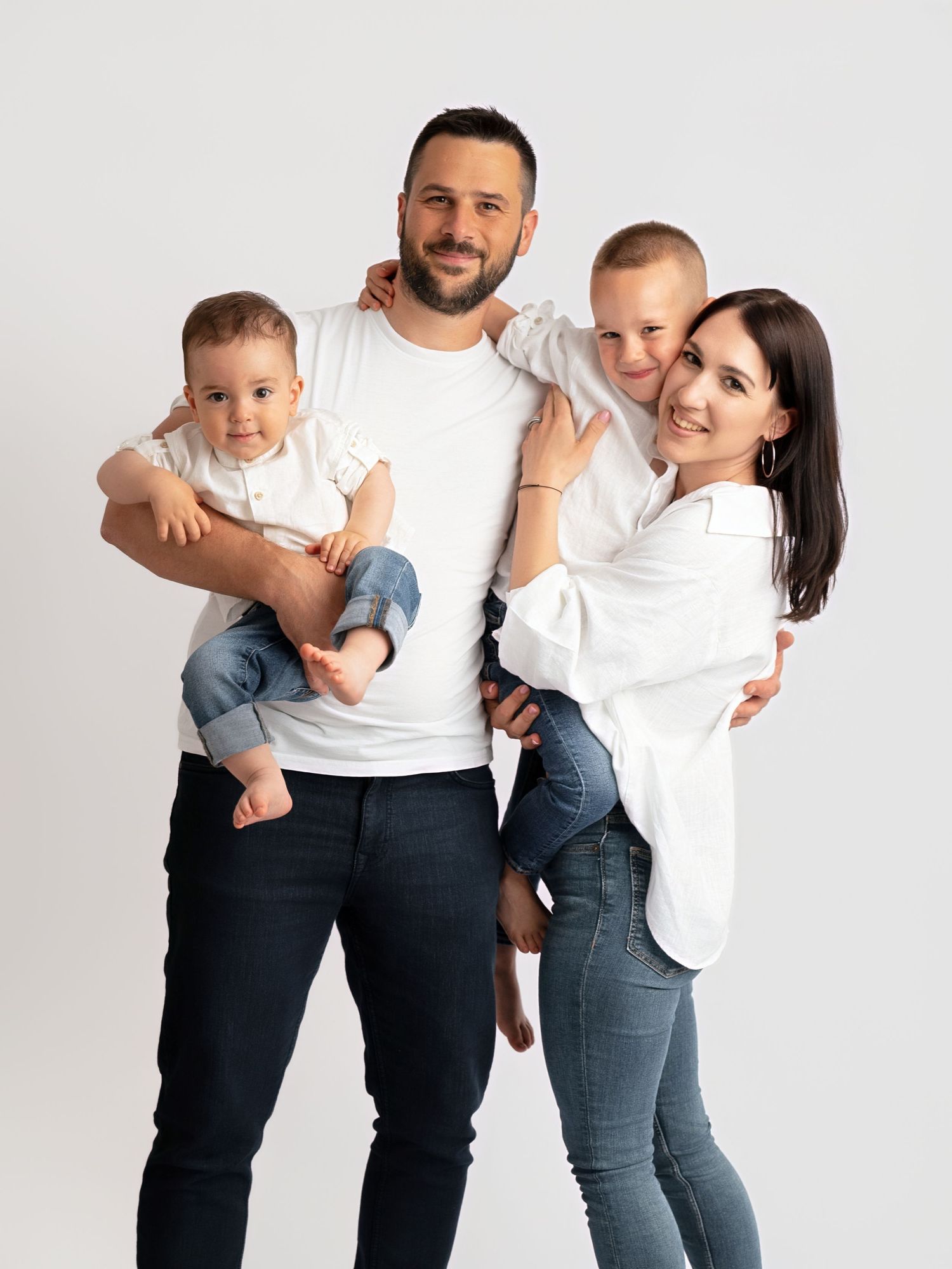 Happy family of four in matching white tops and jeans posing together in a bright studio setting.