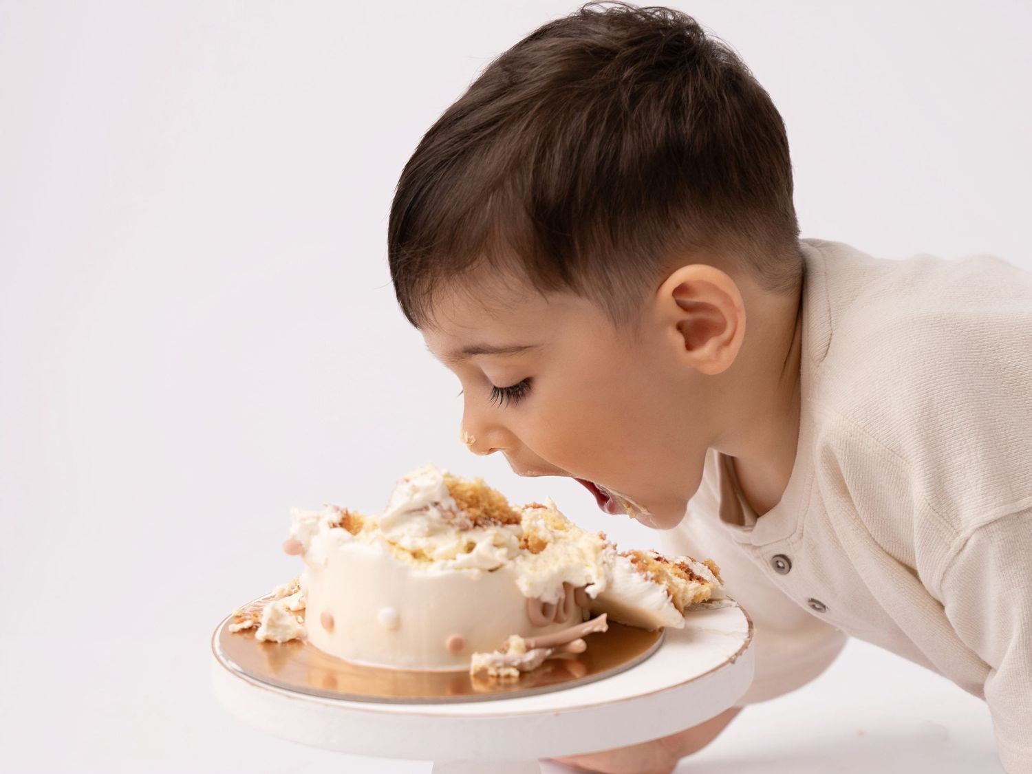 Young boy enthusiastically eating a white frosted cake topped with nuts directly from the plate.