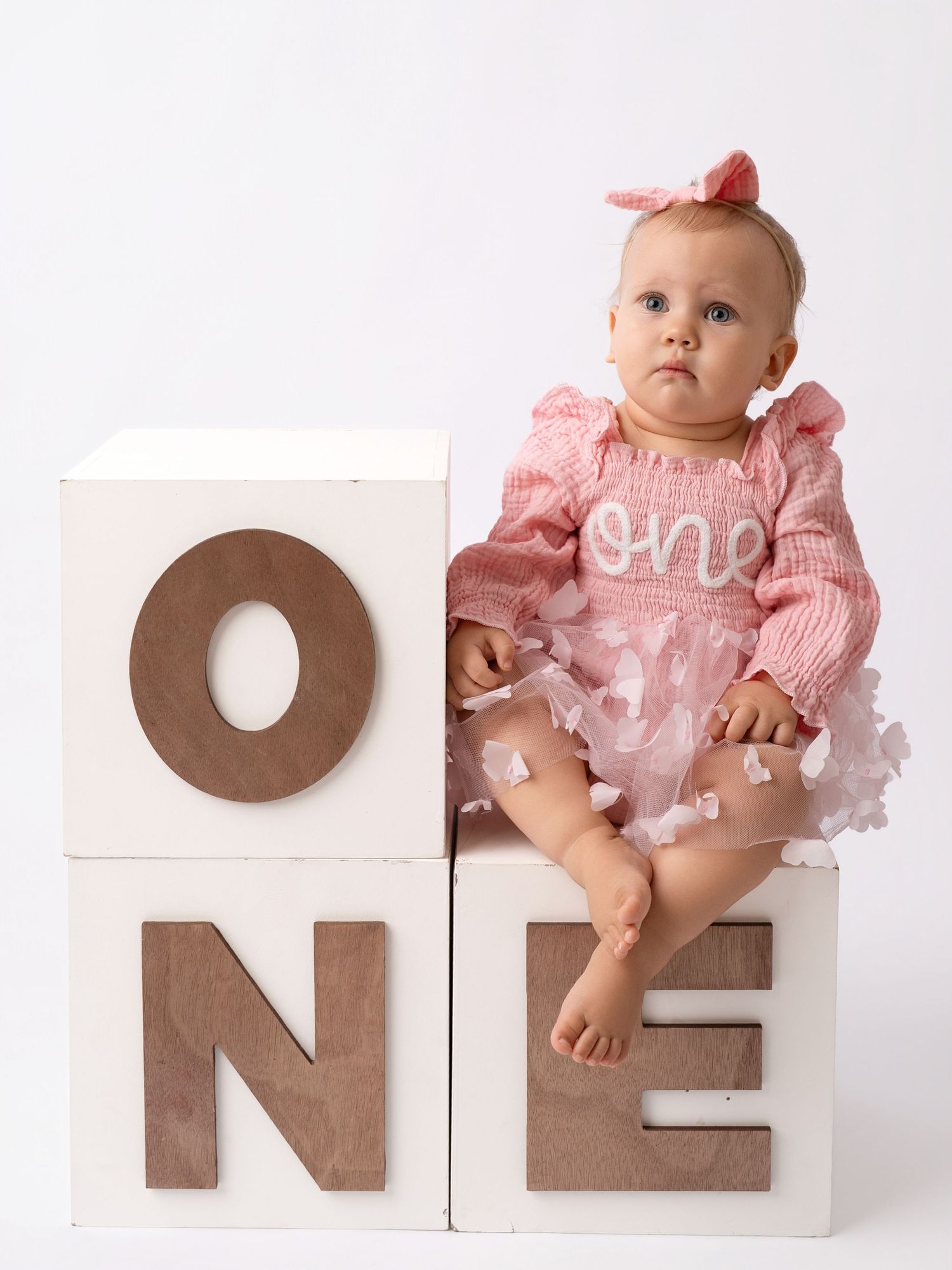 Baby girl in pink dress sits on white ONE blocks for first birthday photo session.