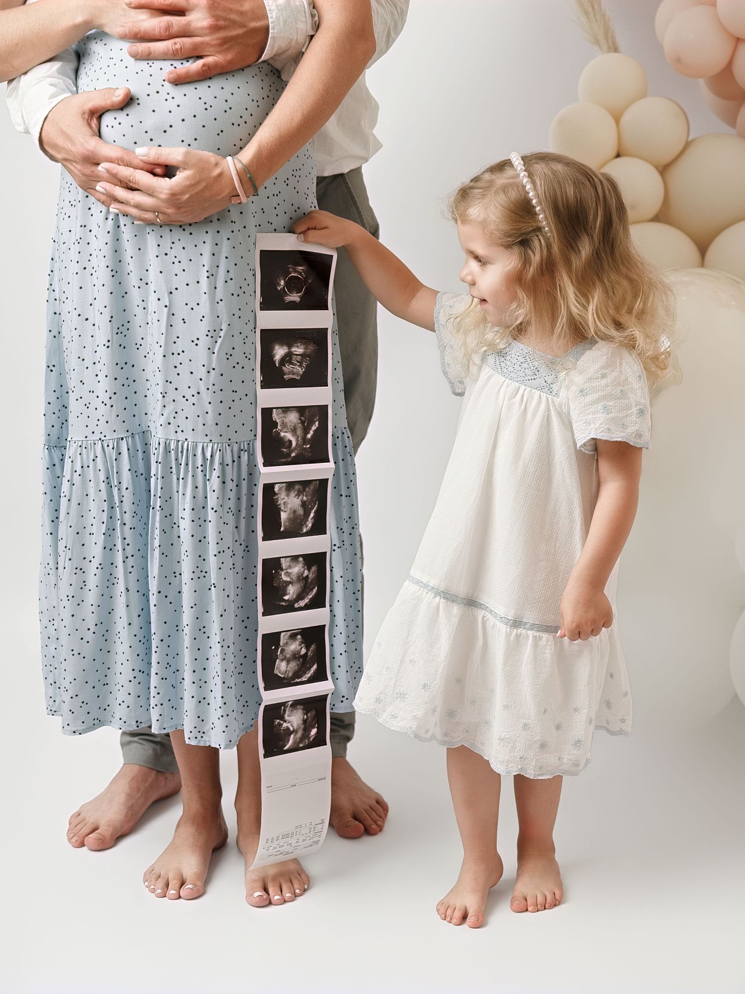 Pregnant woman with partner and young girl holding ultrasound photos during maternity photo session.
