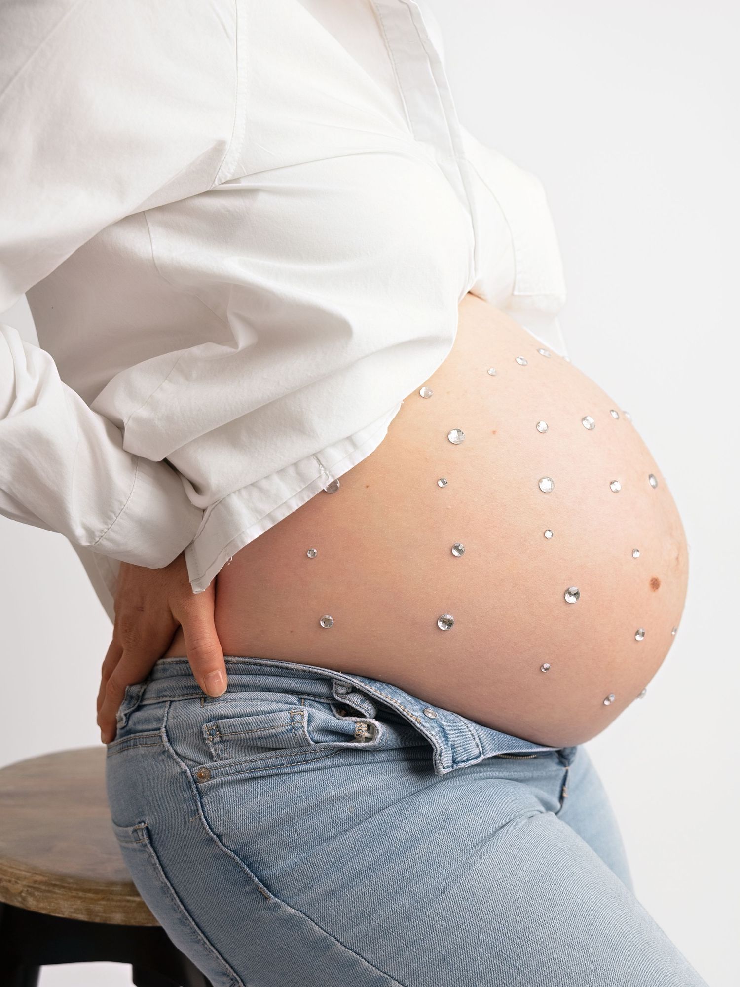 Pregnant woman in white shirt and jeans with rhinestone gems decorating her bare baby bump.