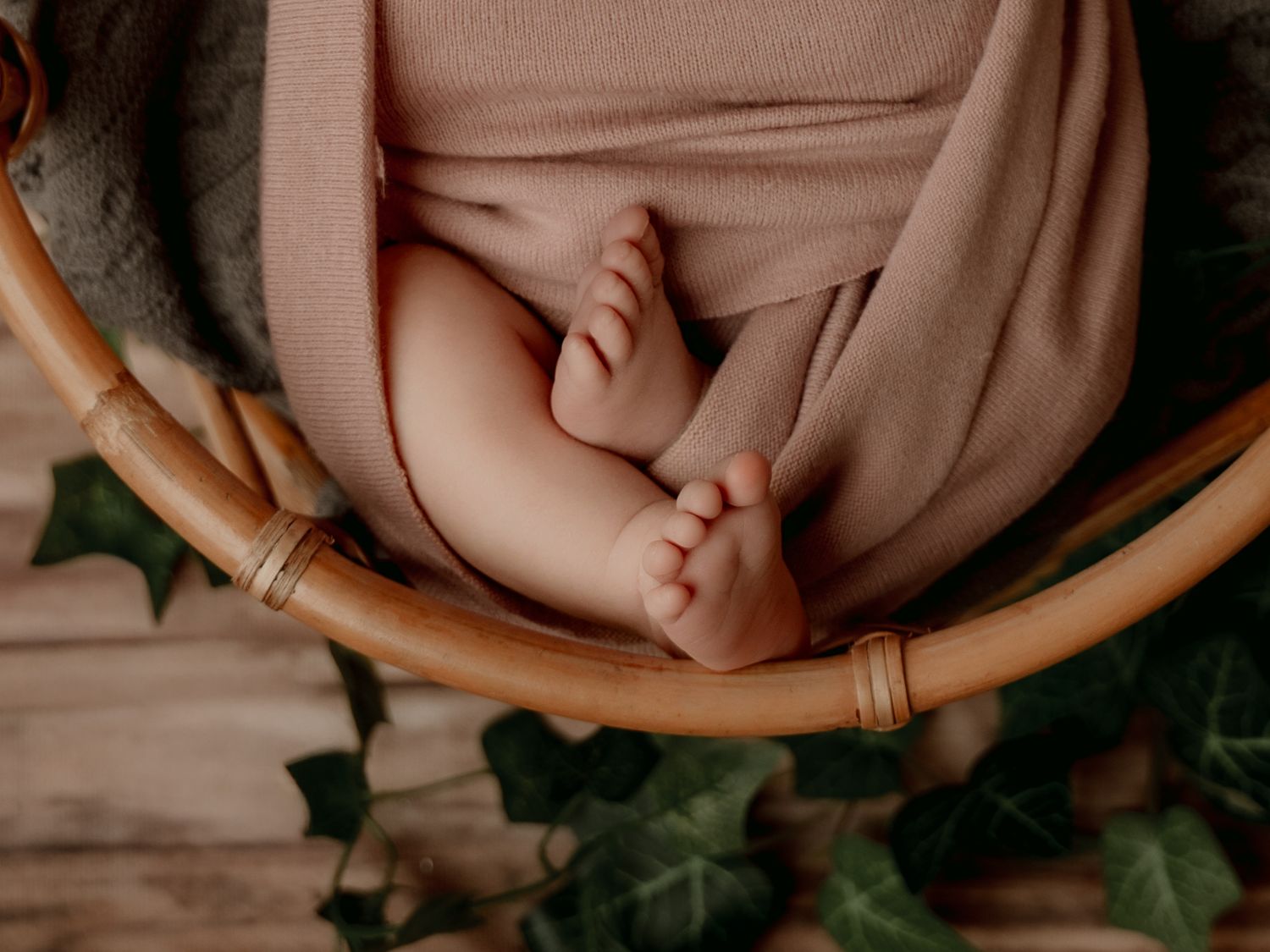 Close-up of a newborn baby's tiny feet and toes resting in a wicker basket with a soft pink wrap.