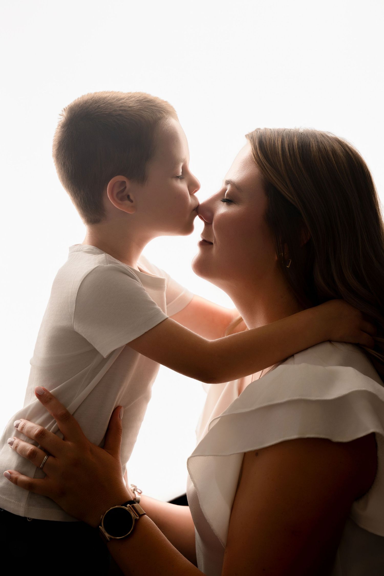 A young boy leans in to touch noses with his smiling mother in a bright backlit portrait.