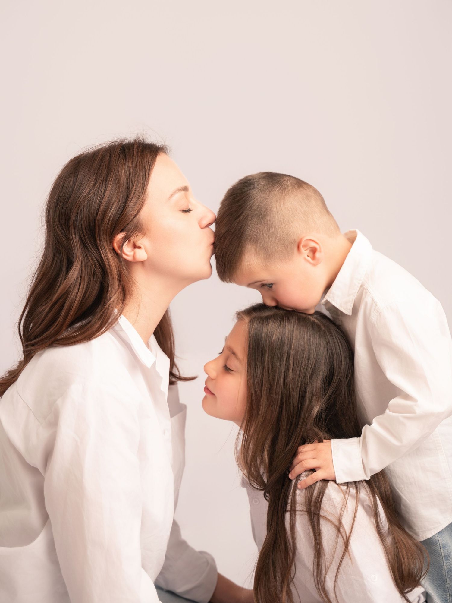 A mother tenderly kisses her son while her daughter leans in during a family studio portrait session.