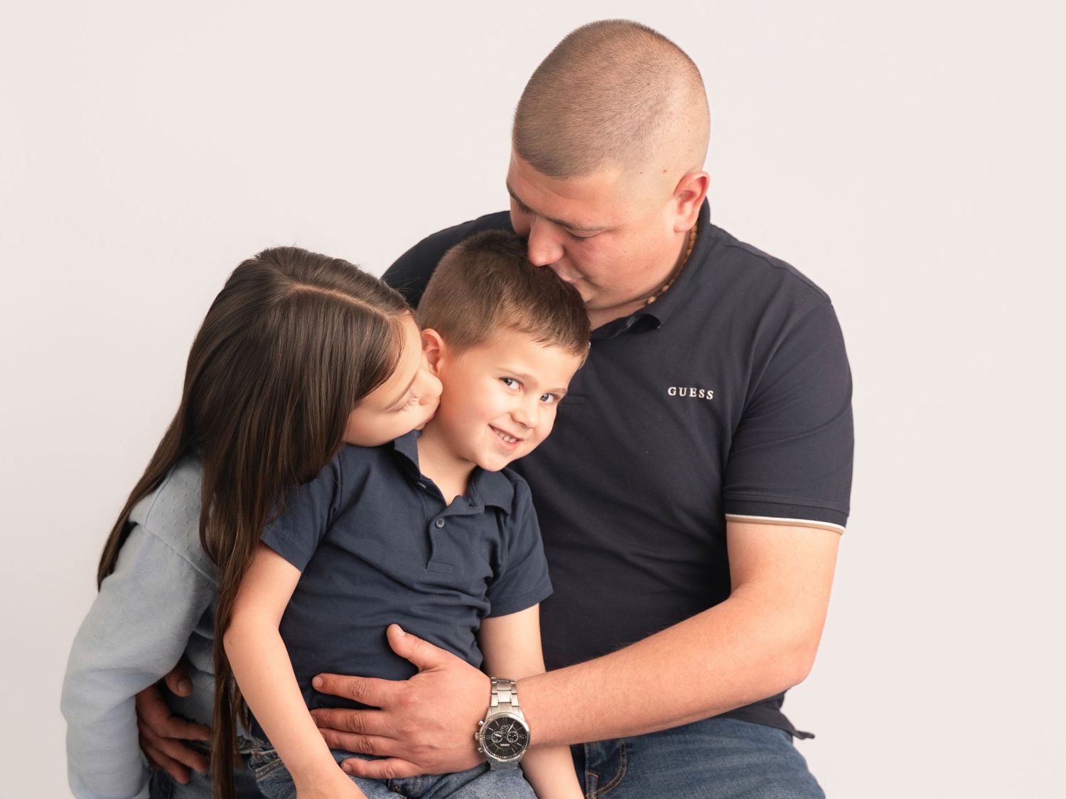 A family portrait of a man and woman lovingly embracing a young boy against a white studio background.