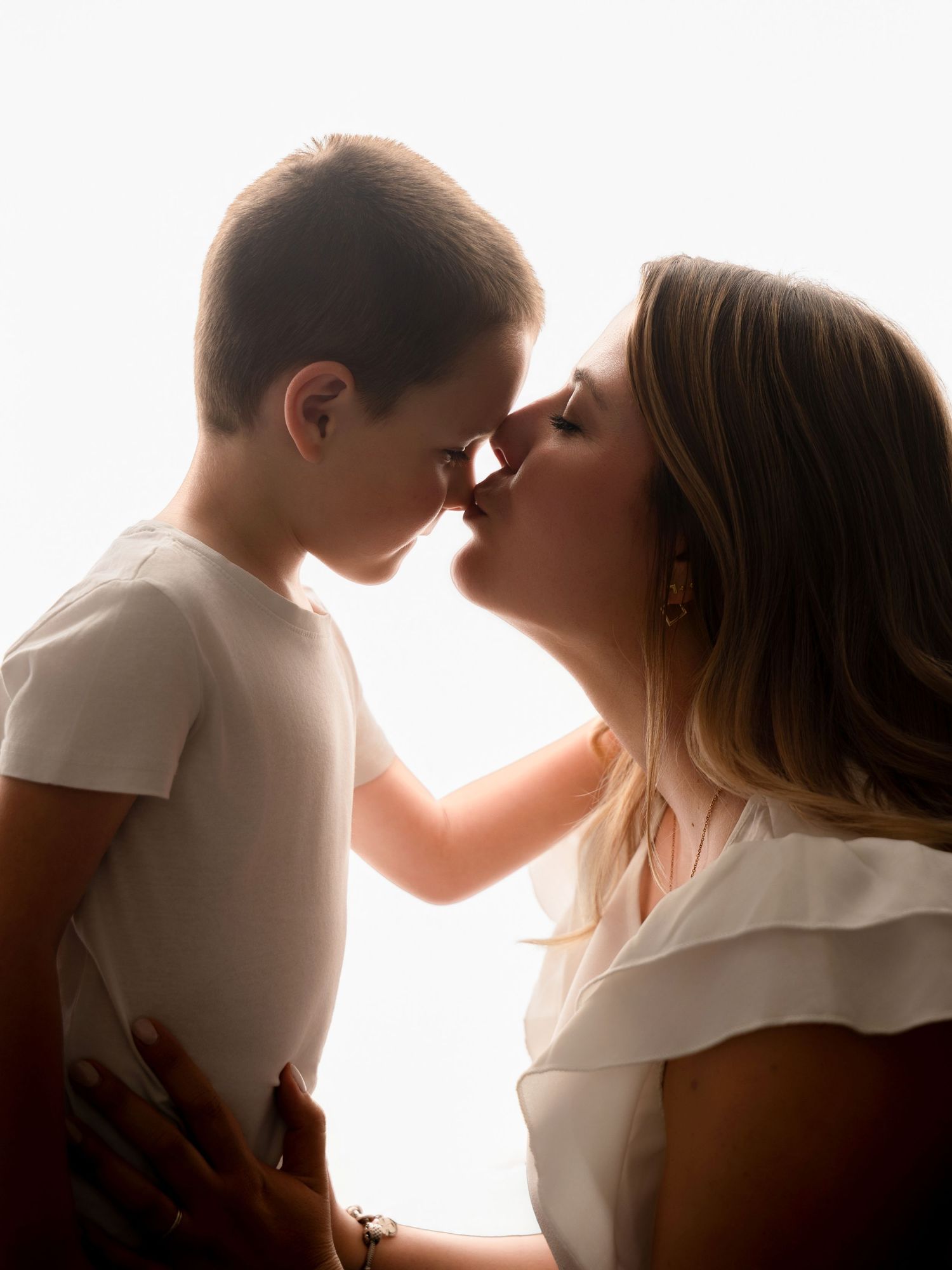 A mother and son share a sweet nose-to-nose moment in soft backlit white light.