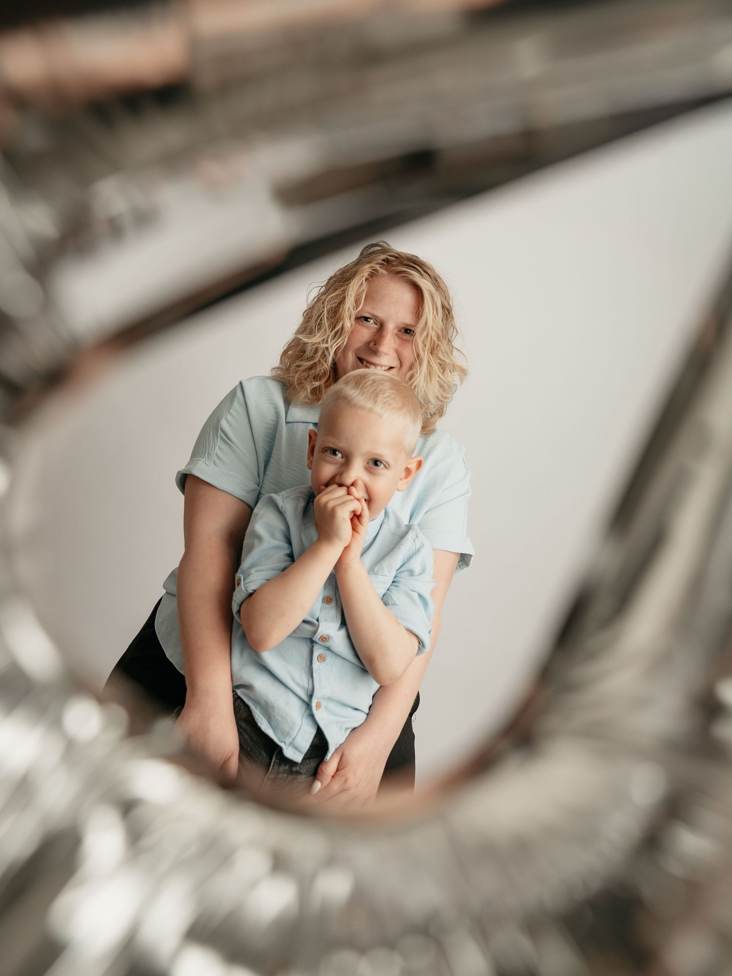 Blonde curly-haired mother hugging young blond son, photographed through a circular frame.