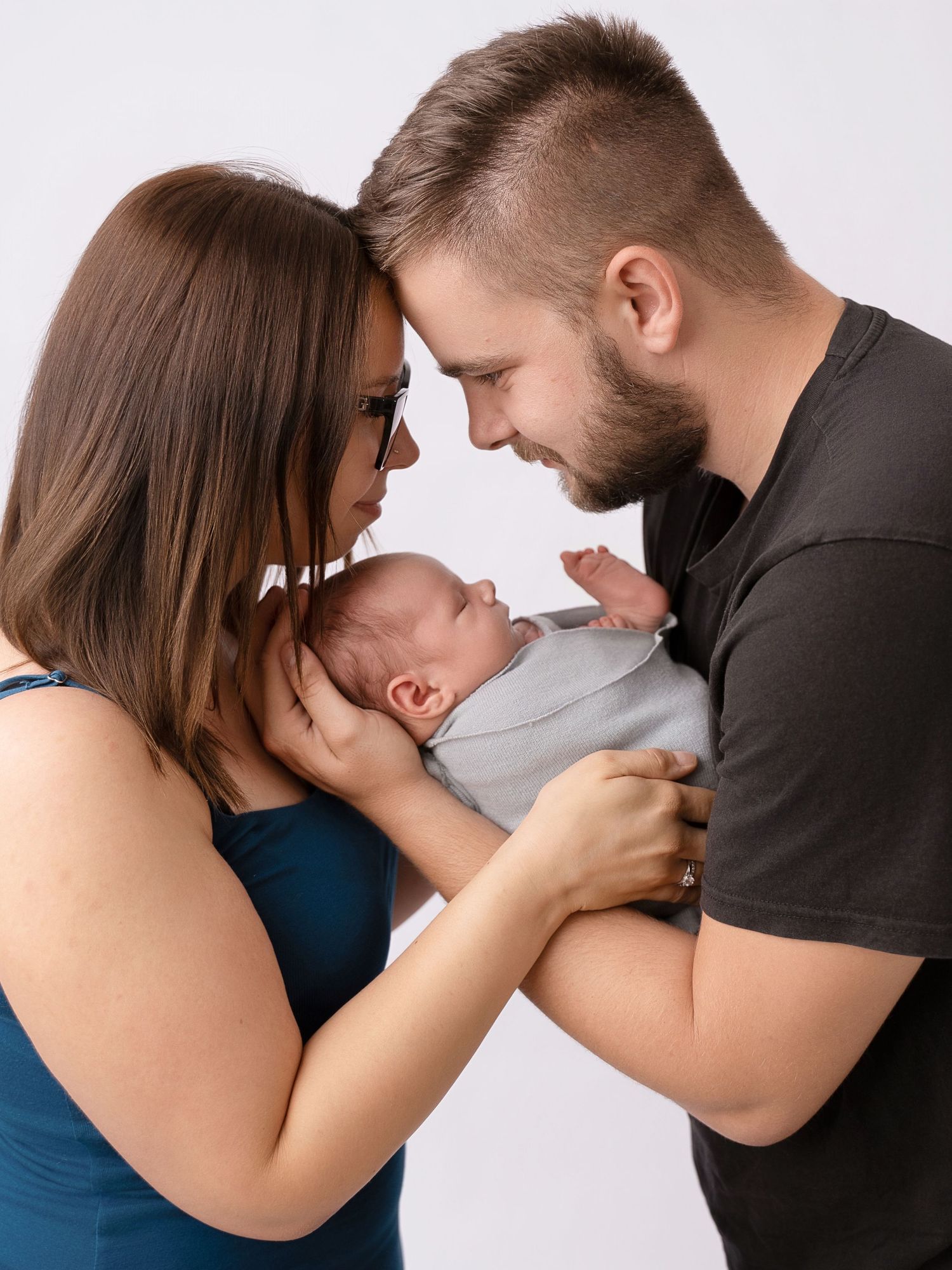 New parents lovingly cradle their sleeping newborn baby together in a tender family portrait studio photo.