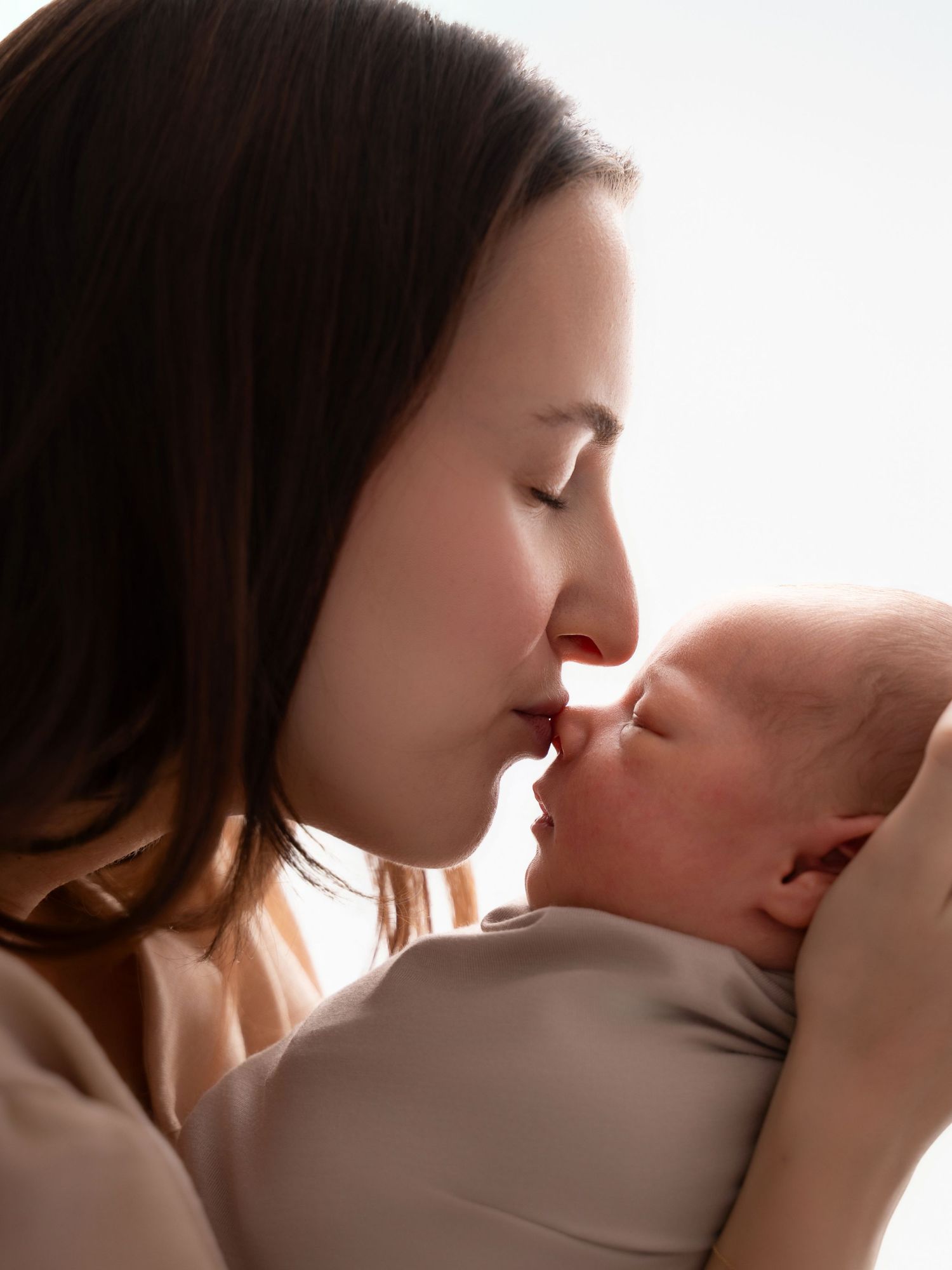 A mother tenderly kisses her newborn baby, sharing an intimate moment in soft, warm lighting.