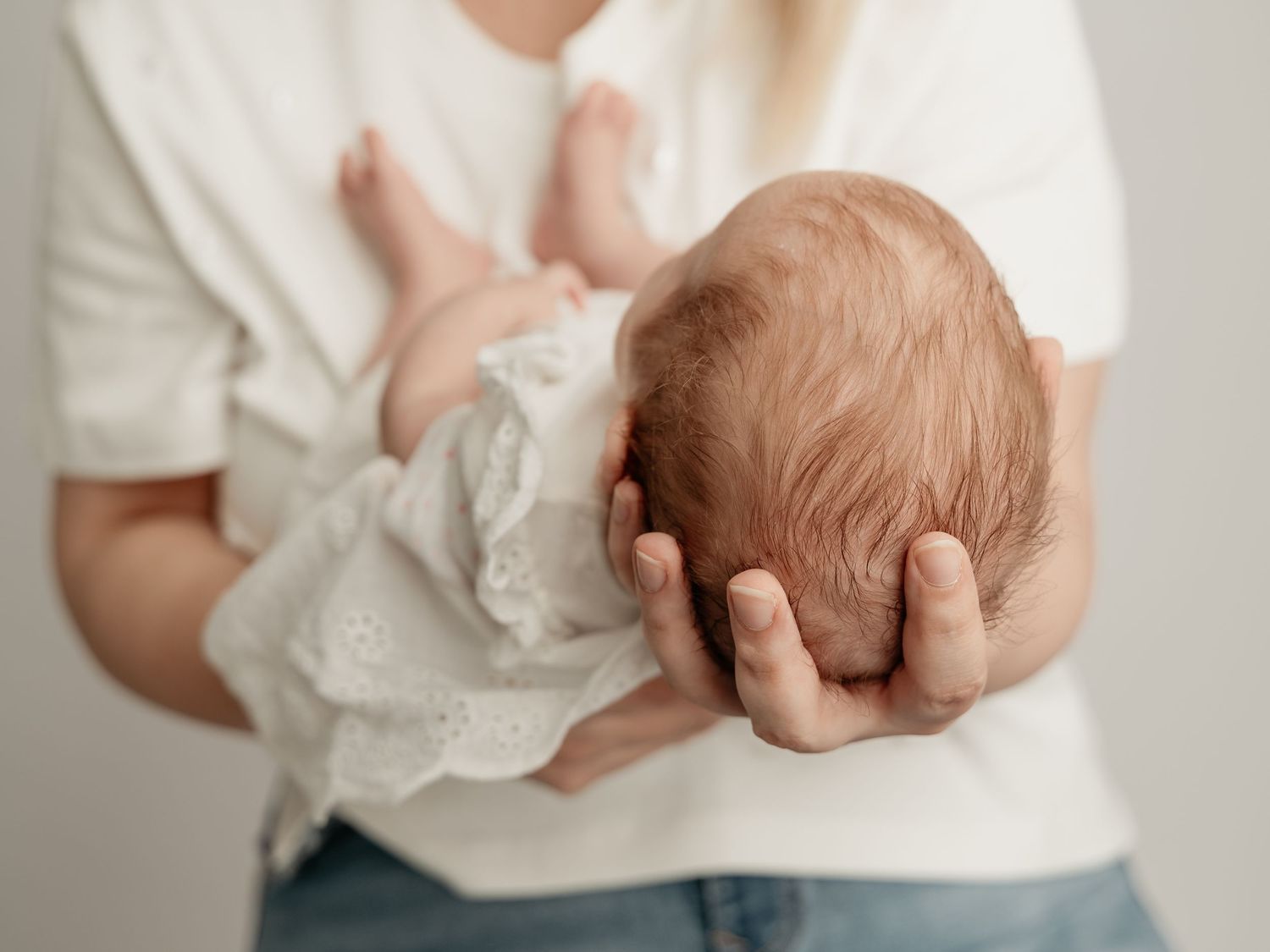 Adult cradling a newborn baby wrapped in white lace cloth.