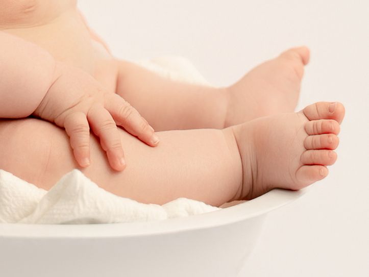 Close-up of chubby baby feet and hands resting in a white bowl during a studio photo session.