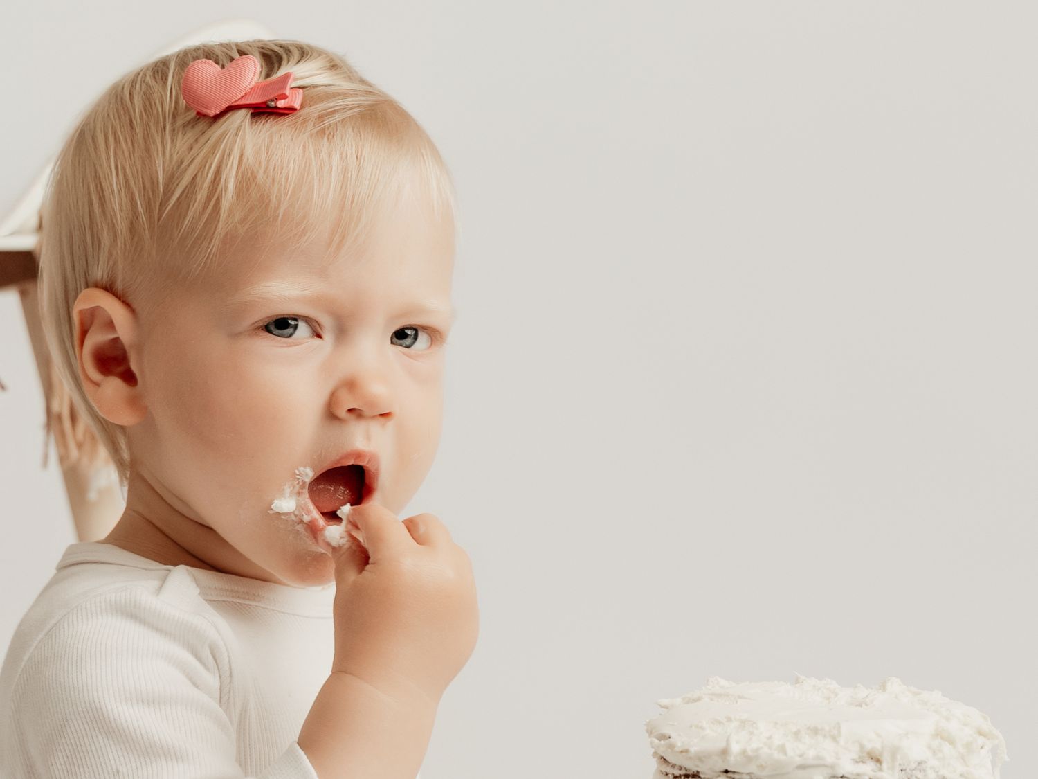 Cute blonde baby girl with pink bow eating cake during a first birthday cake smash photoshoot.