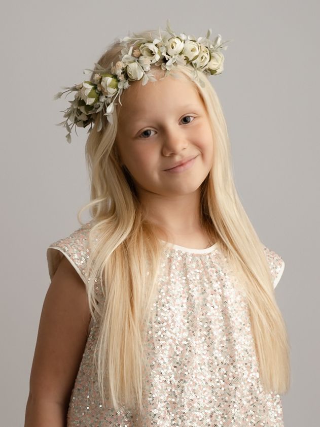 Smiling blonde girl wearing a floral crown and sequined dress in a soft studio portrait setting.