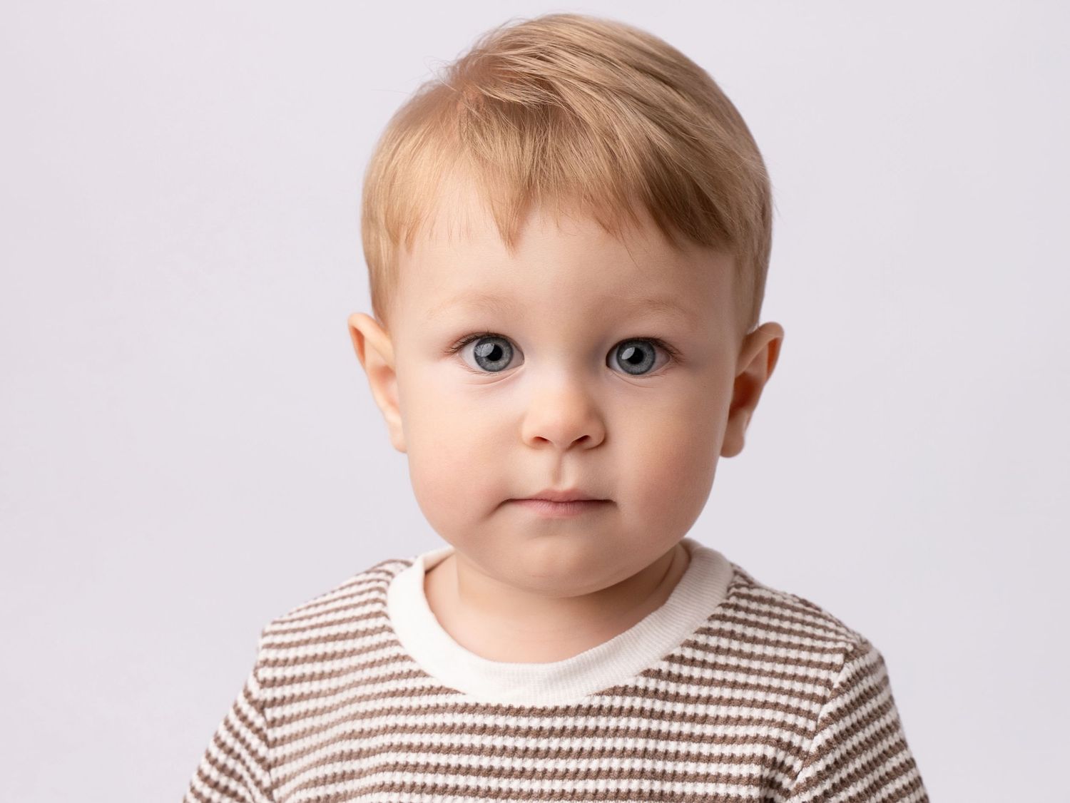 Cute toddler boy with blue eyes and blonde hair wearing a striped shirt, studio portrait photo.