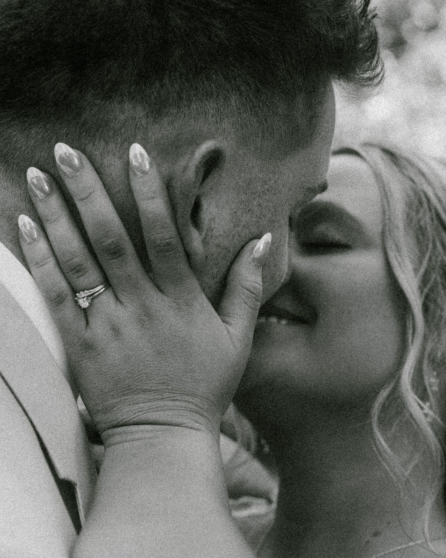 Black and white photo of a couple sharing a romantic kiss, bride wearing an engagement ring with manicured nails.