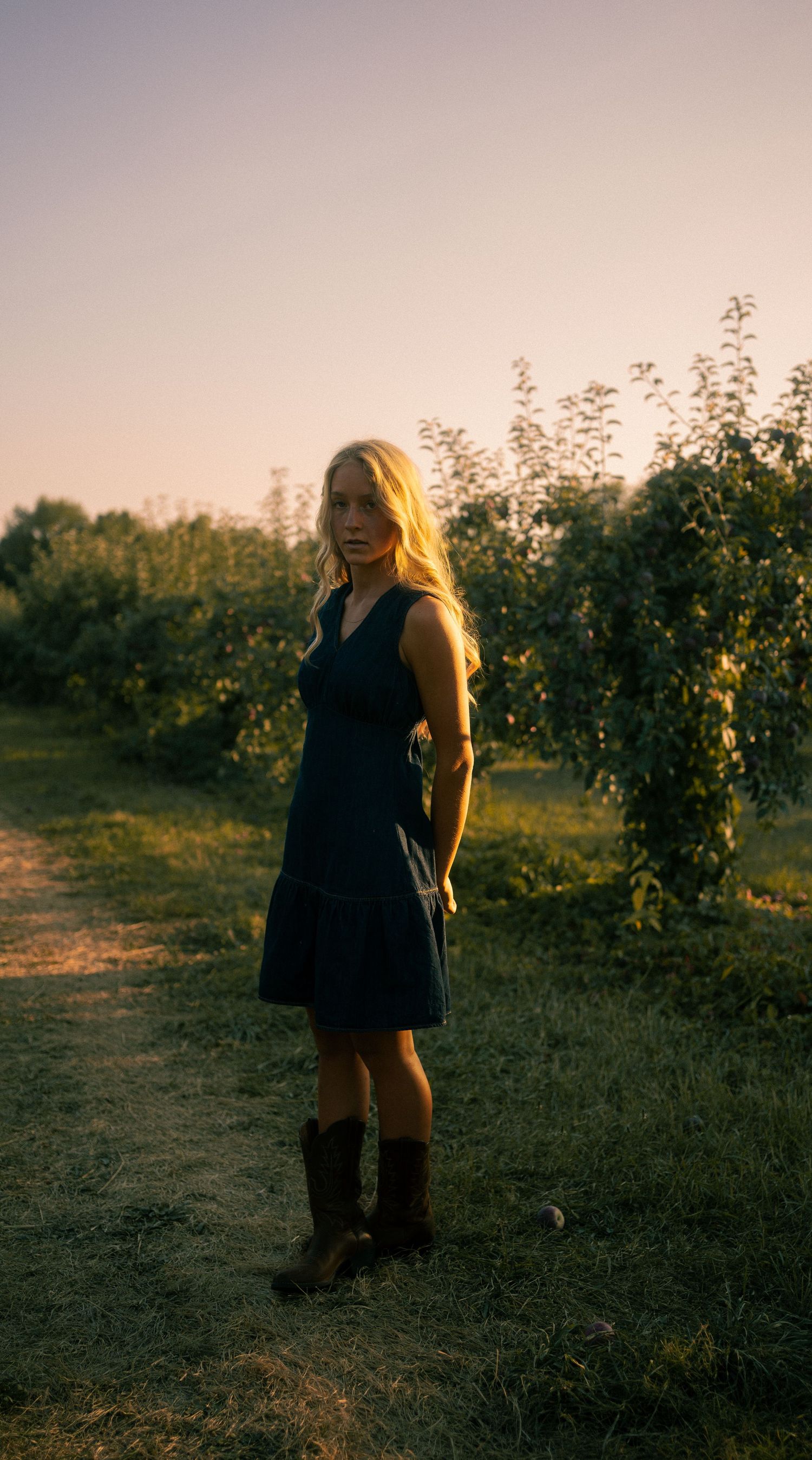 A silhouette of a person in a black dress standing in a field at golden hour.