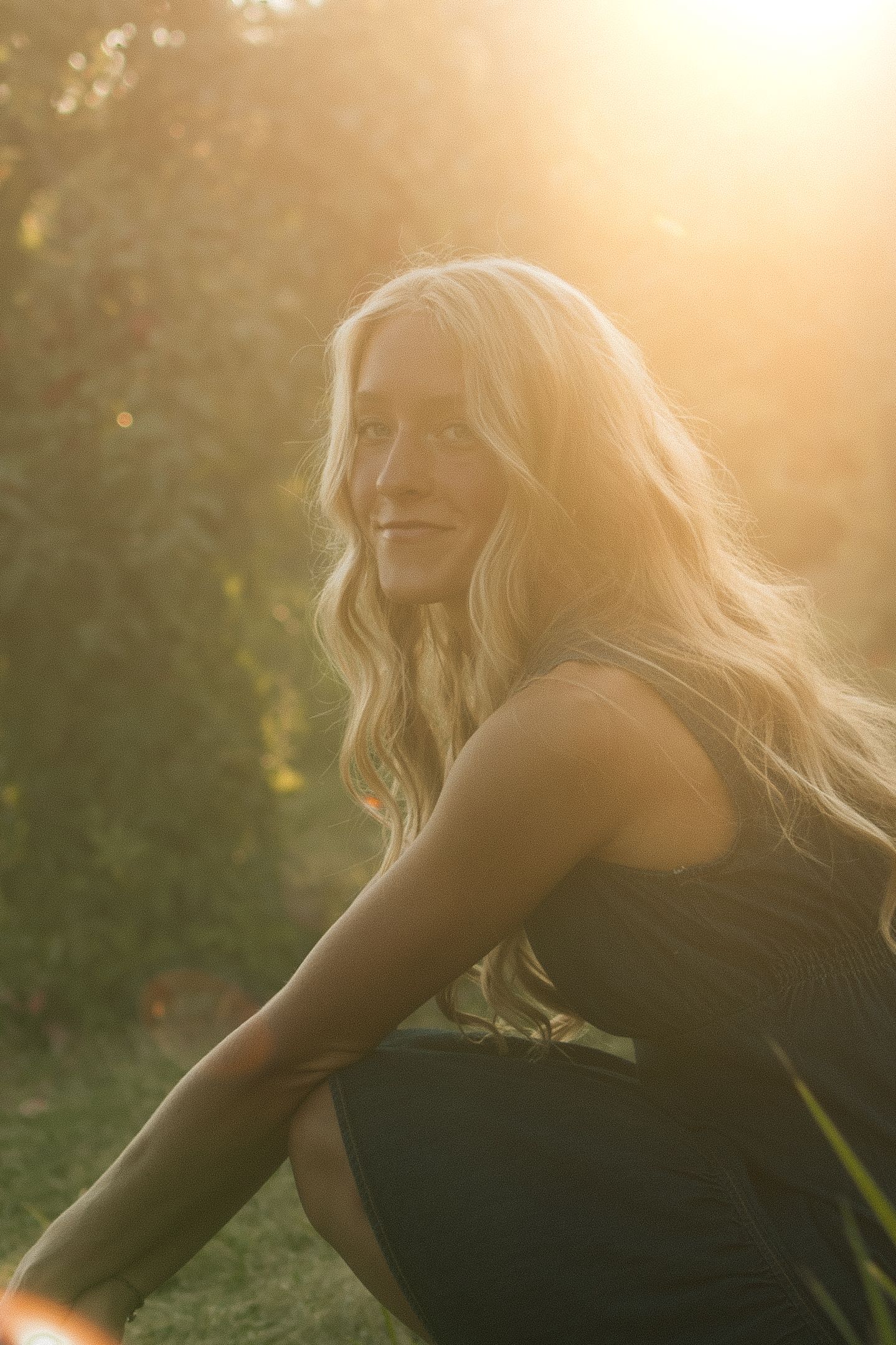A backlit portrait in golden sunlight showing flowing blonde hair against natural foliage.
