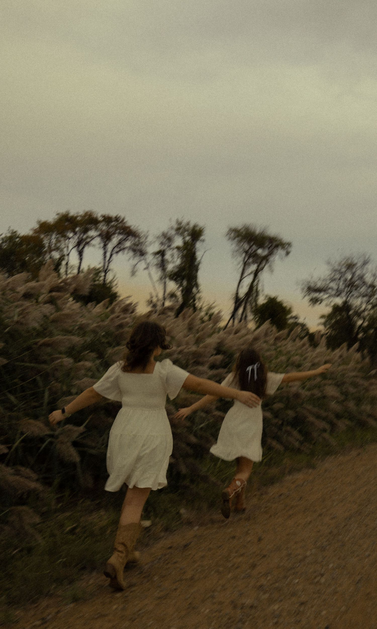Two people running up a hillside trail at sunset with arms outstretched.