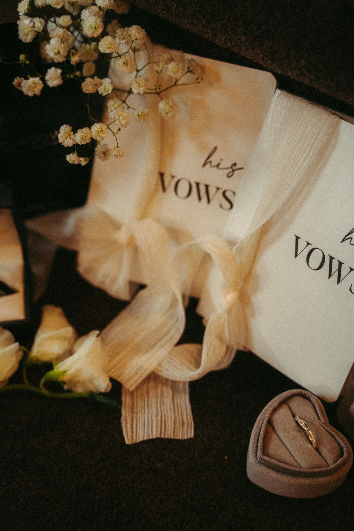 Wedding vows book with delicate white flowers and wooden ring box displayed in romantic vintage style lighting.