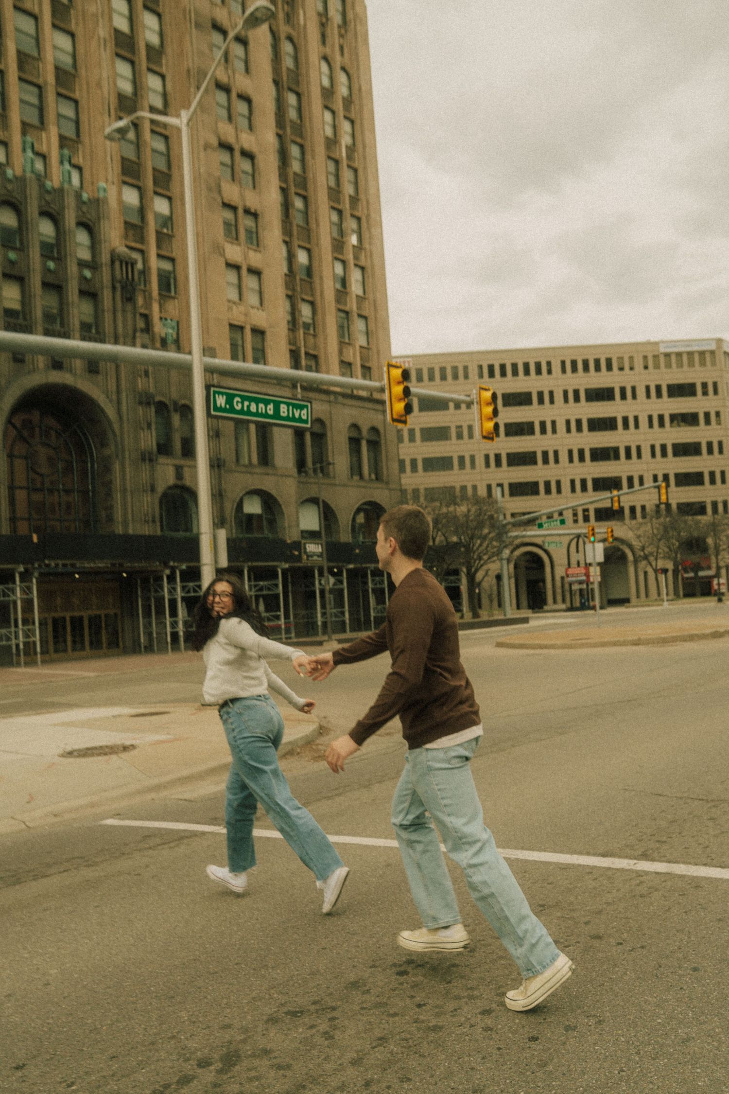 Couple holding hands and crossing a street on W Grand Blvd in Detroit, Michigan on a cloudy day.