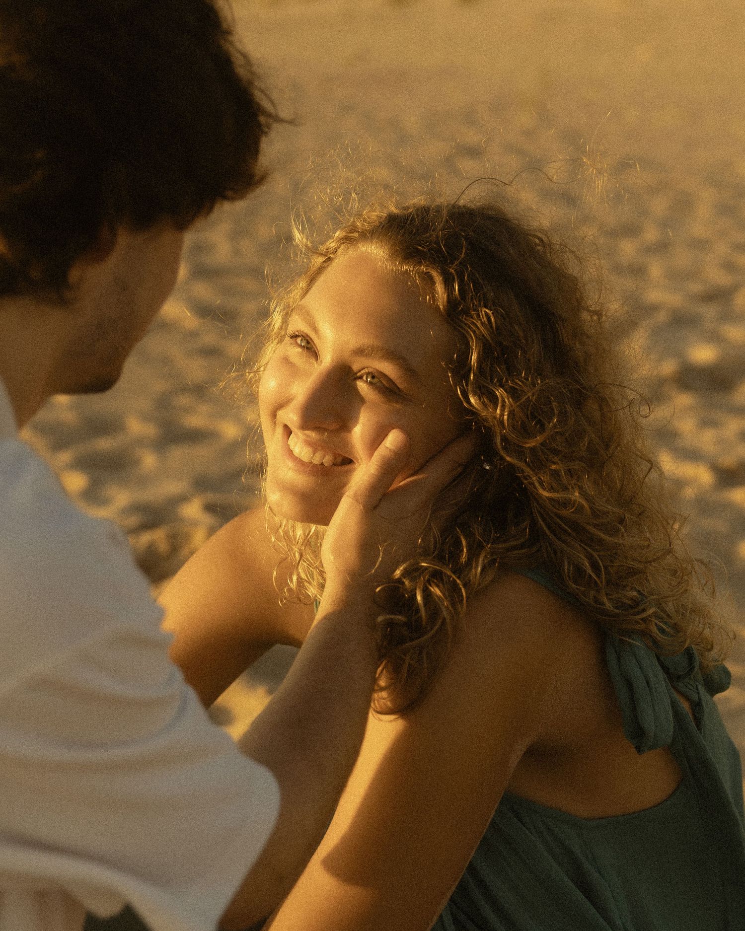 A couple shares a tender moment on a sandy beach at golden hour, man gently touching woman's face.