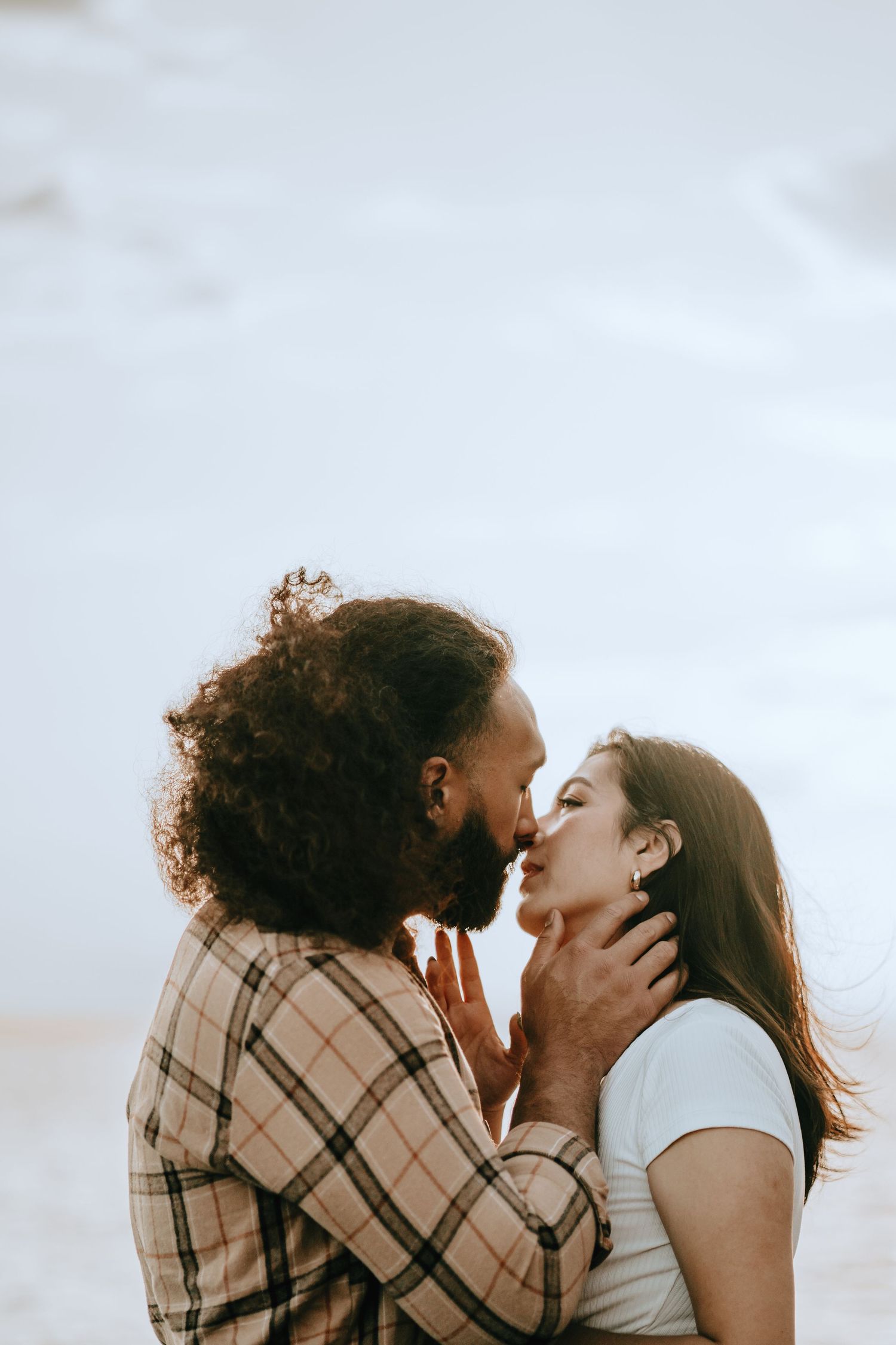 Passionate couple sharing a kiss outdoors, man with curly hair holding woman's face gently.