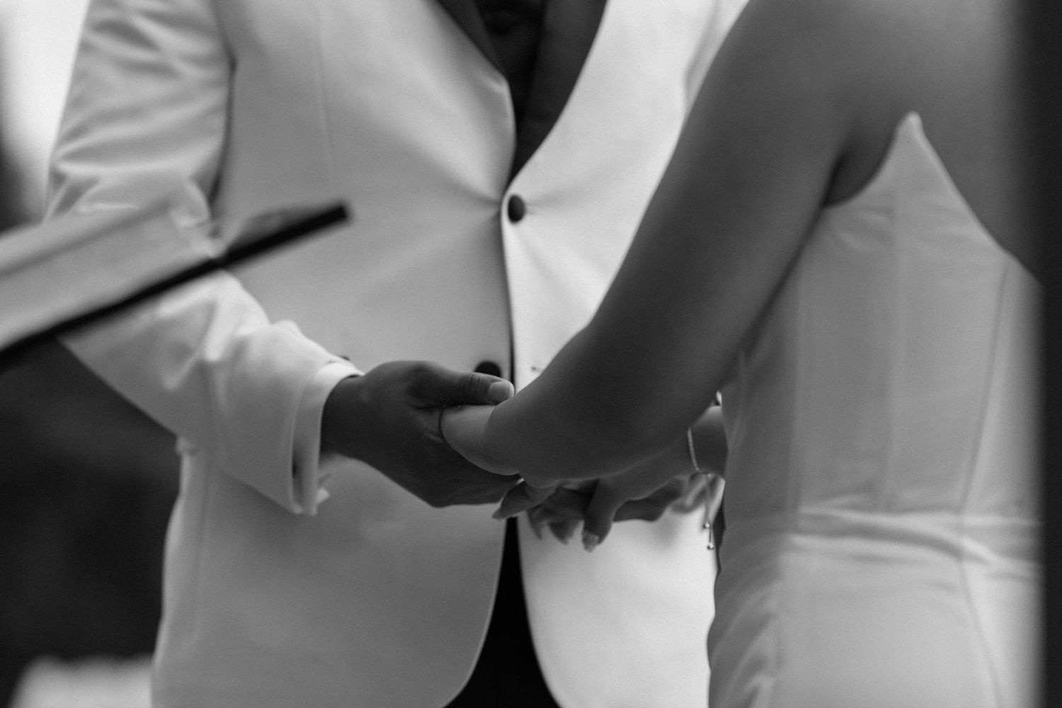 Black and white close-up of a bride and groom holding hands during their wedding ceremony.