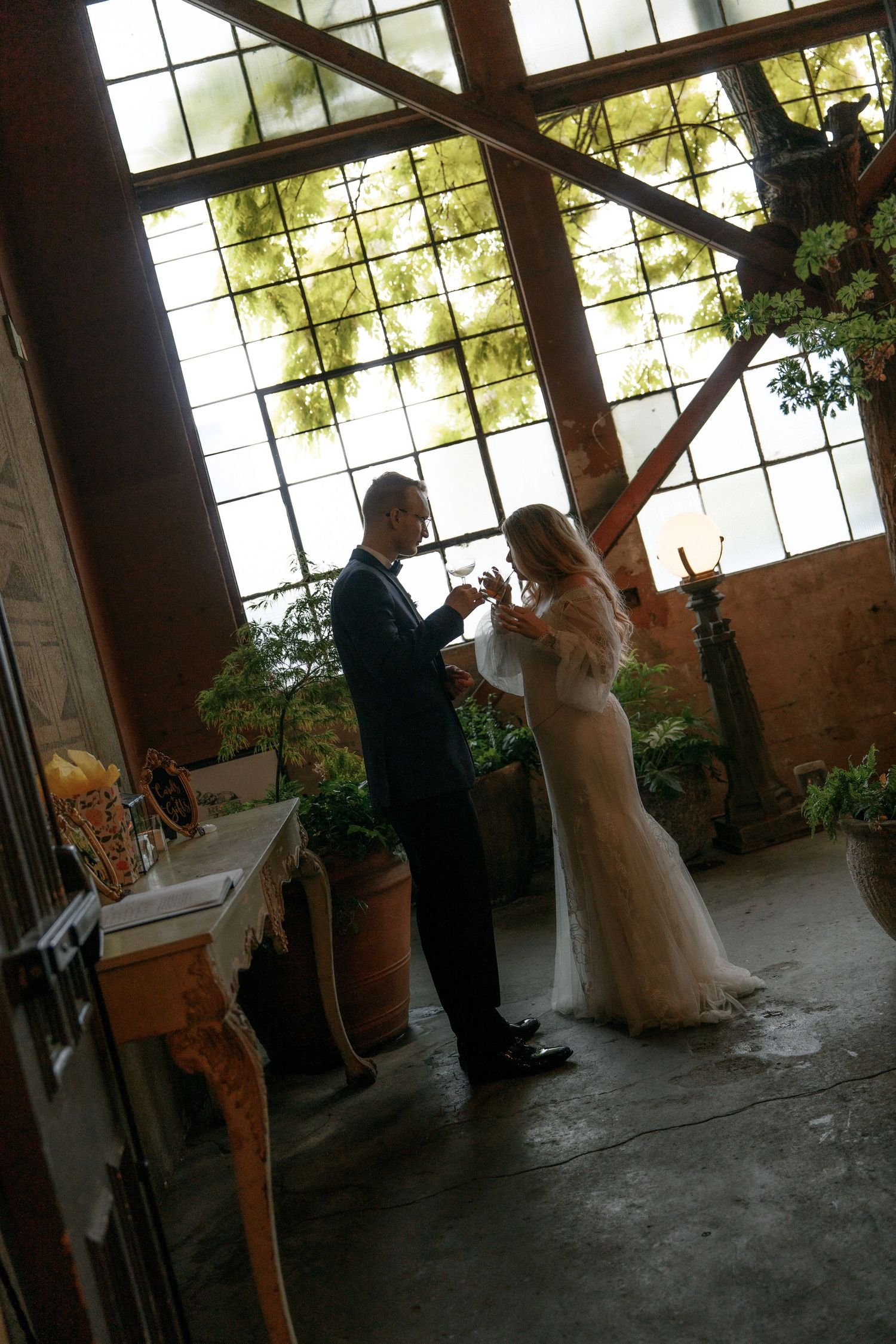 Bride and groom share first dance in elegant venue with large industrial windows.