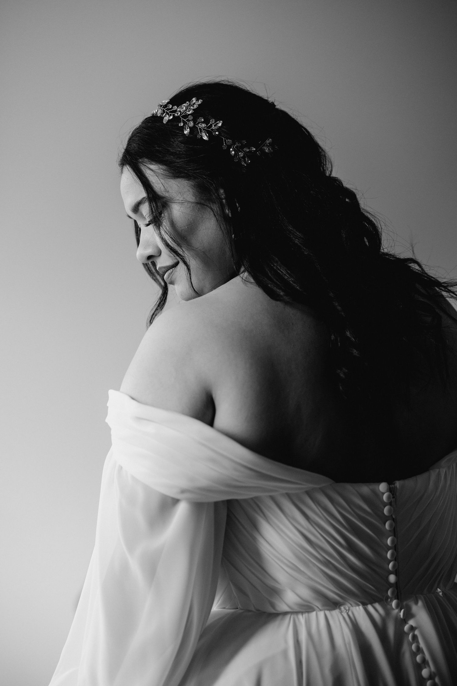 Elegant black and white portrait of a bride from behind showcasing her floral hair piece and off-shoulder gown.