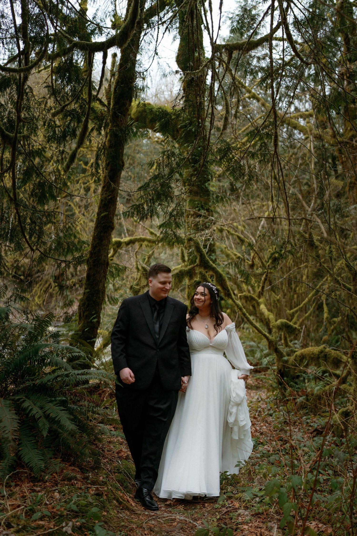 Laughing bride and groom stroll together through a beautiful moss-draped forest on their wedding day.