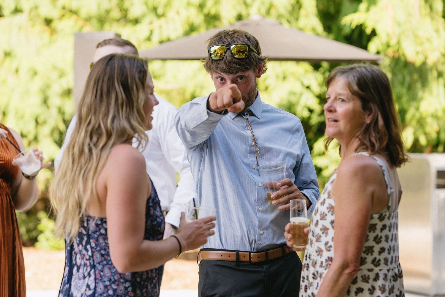 Wedding guests socializing and drinking outdoors in a sunny garden setting.