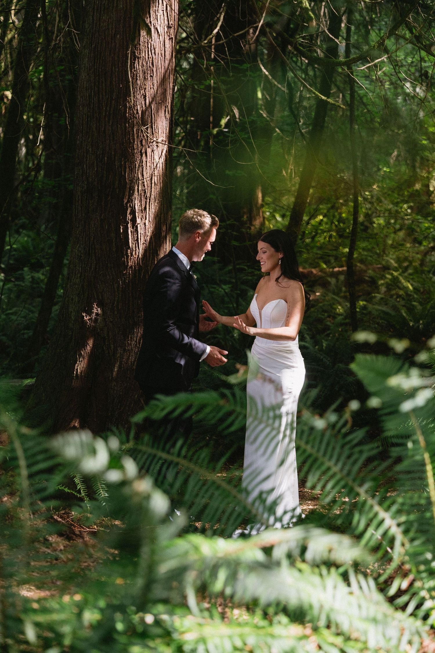 Bride and groom share a tender moment among ferns in forest.