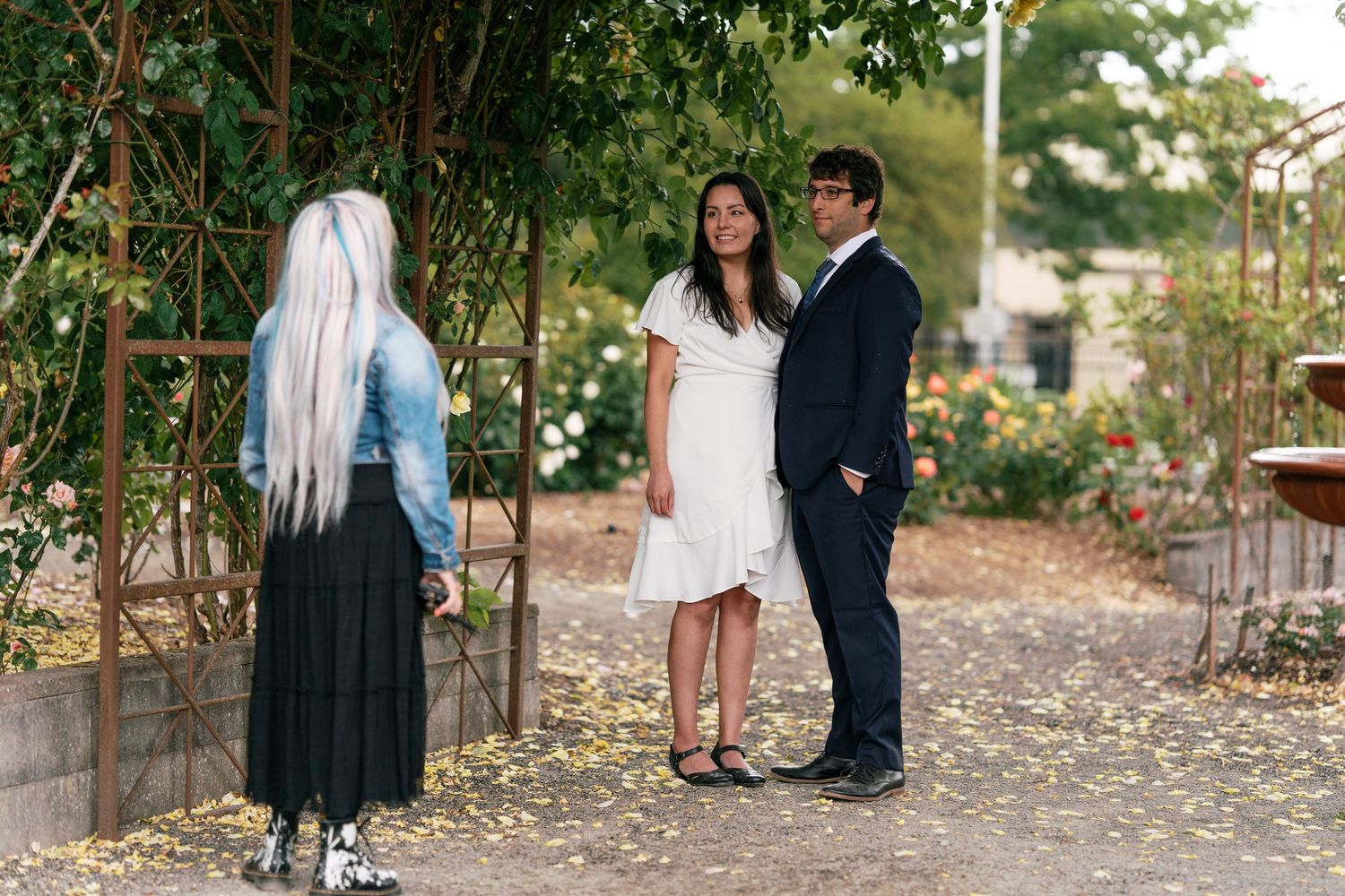 Officiant meeting with couple on a flower-lined garden path before wedding ceremony.