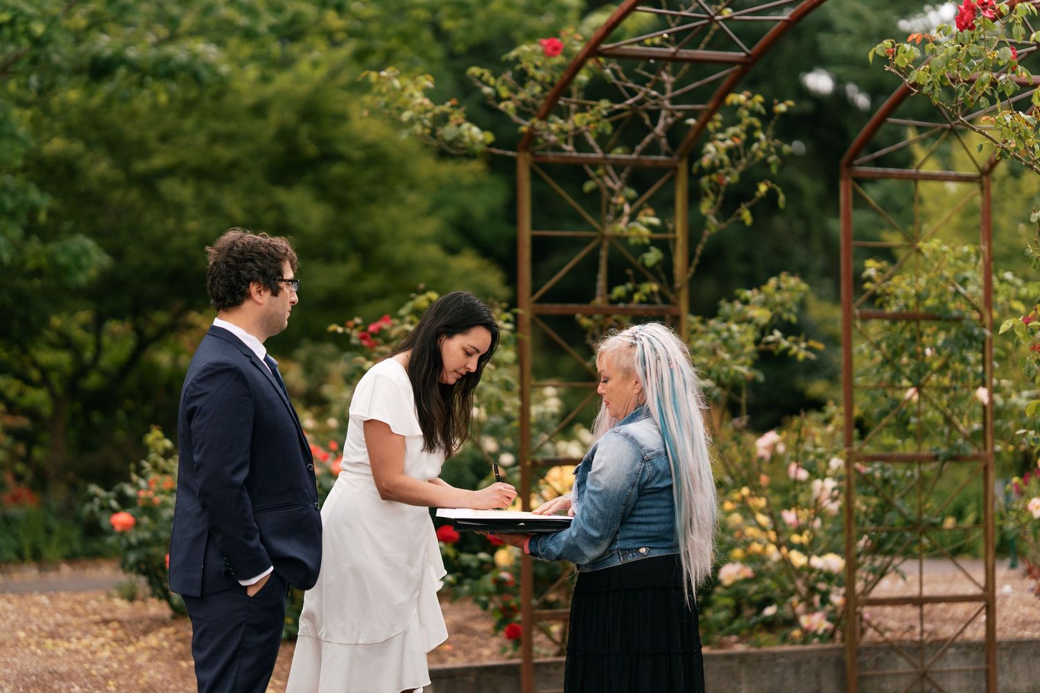 Couple exchanging vows with officiant under rose garden arbor during intimate elopement.