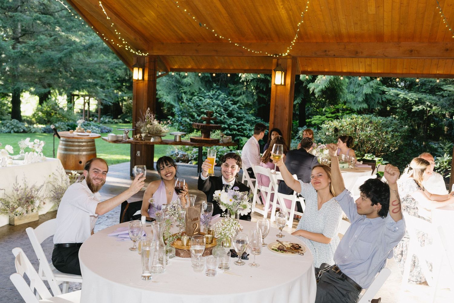 Wedding guests raise glasses in a toast at a beautifully decorated outdoor reception table.
