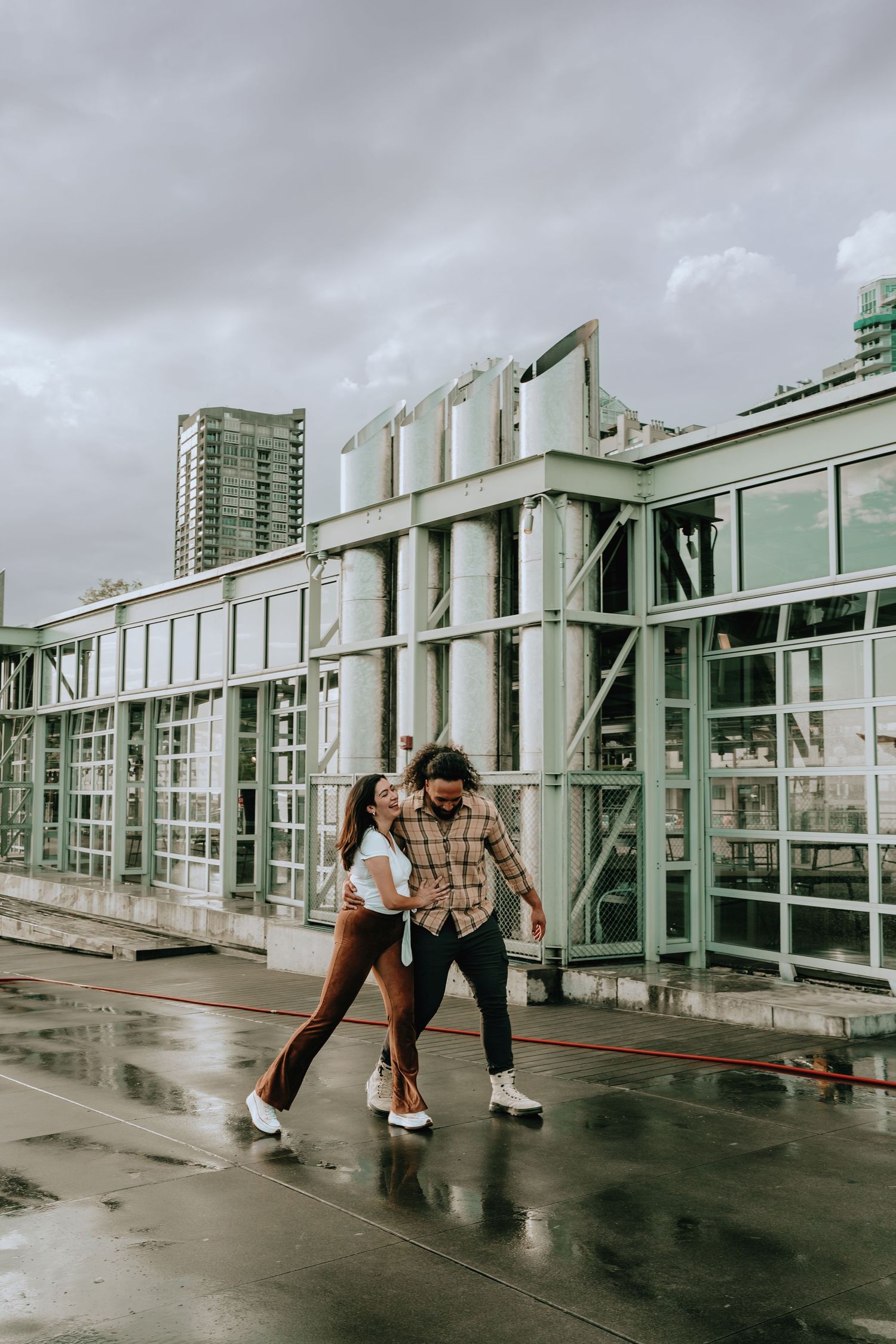 Couple walking together on a wet rooftop terrace with Seattle city skyline in background.