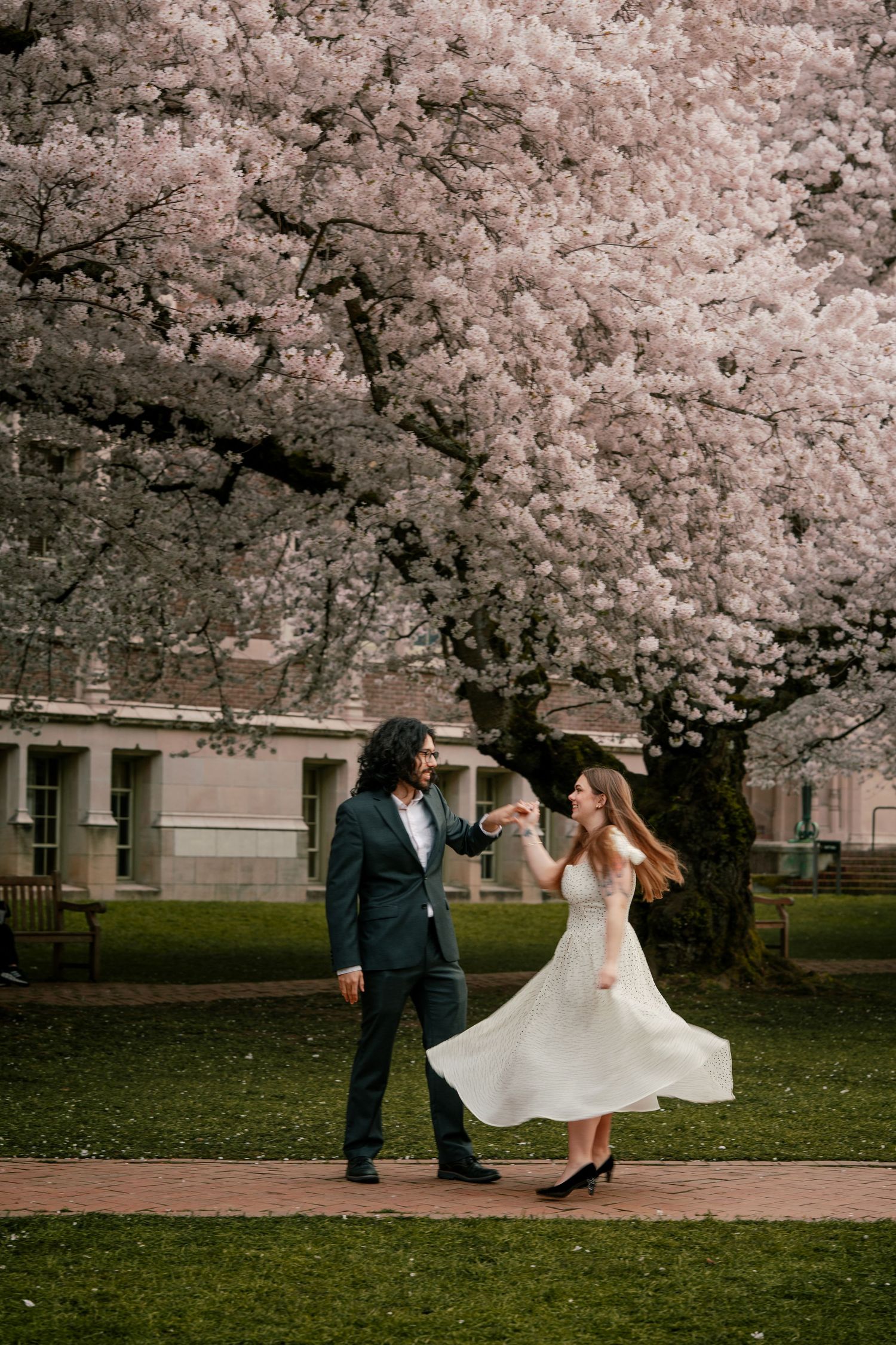 Joyful couple dancing under blooming cherry blossom trees in a lush green park setting.