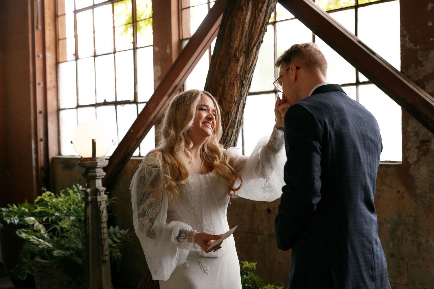 Bride laughs joyfully while touching groom's face during intimate wedding ceremony exchange.