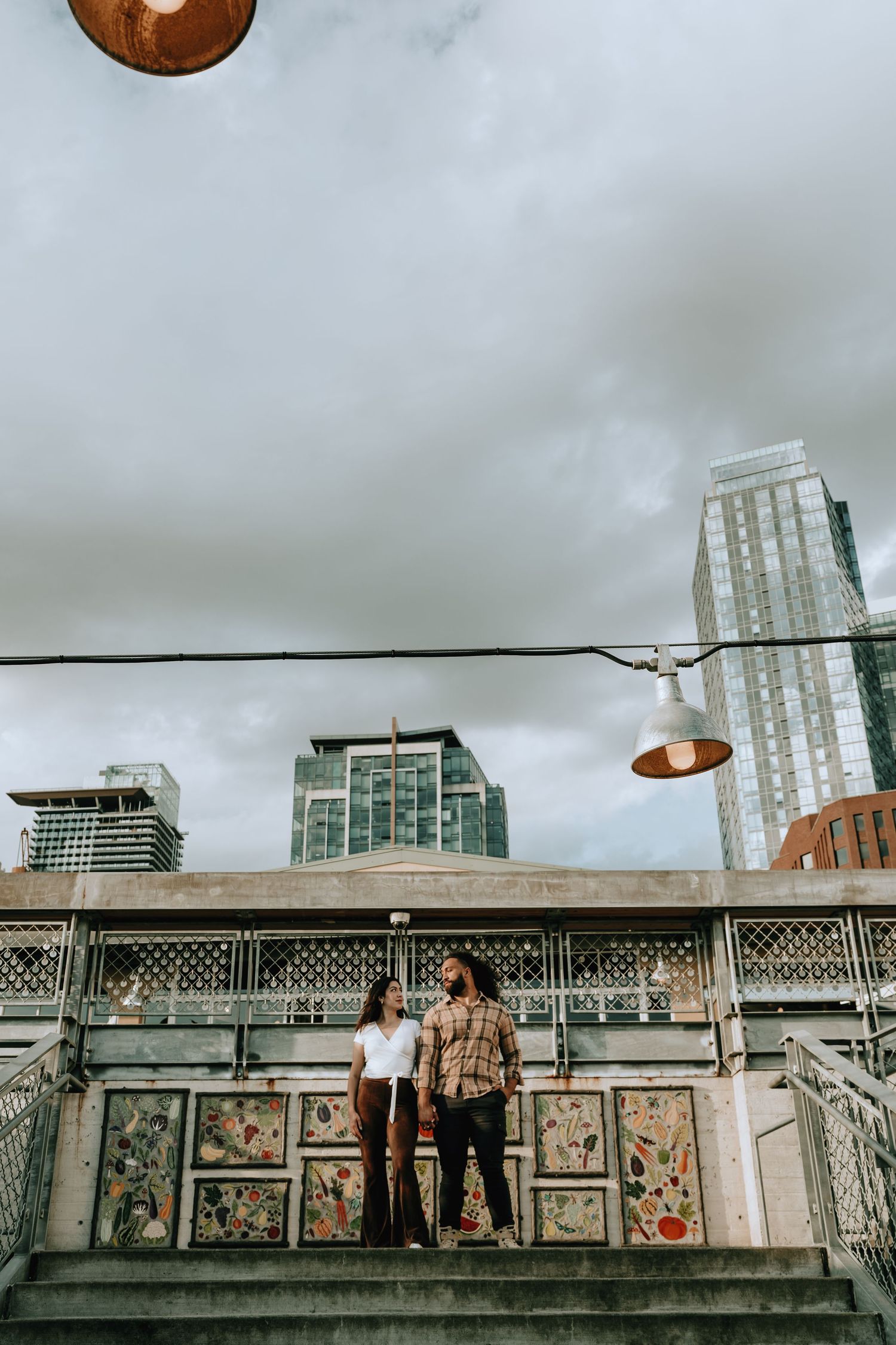 Couple standing on decorated steps with Seattle skyscrapers and cloudy sky in background.