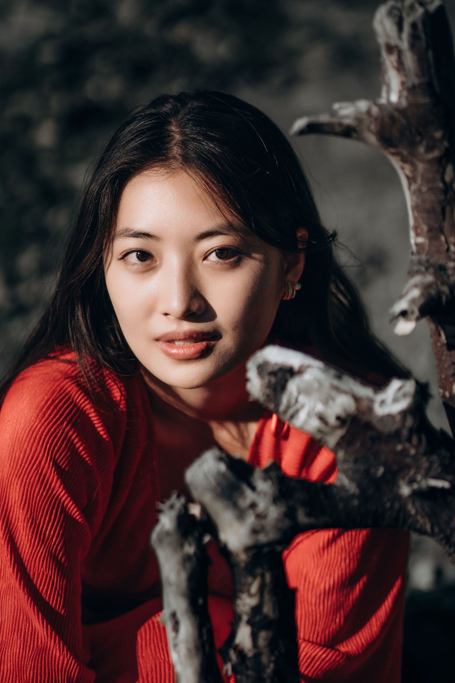 Young woman in red sweater posing beside weathered driftwood branches outdoors.