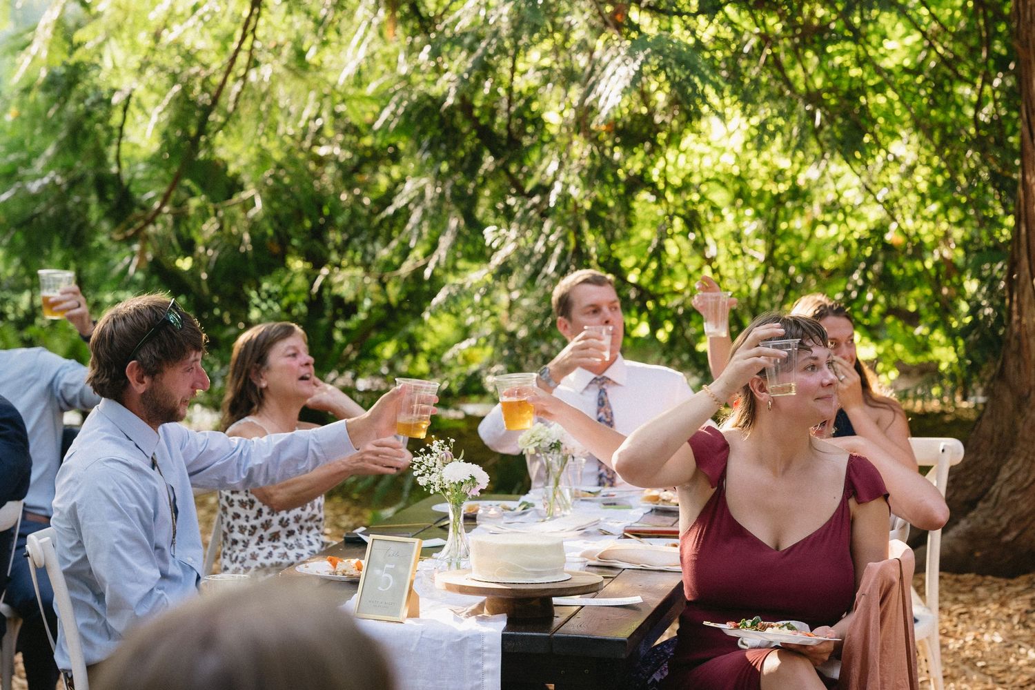 Wedding guests raising glasses in a toast at an outdoor garden reception table.