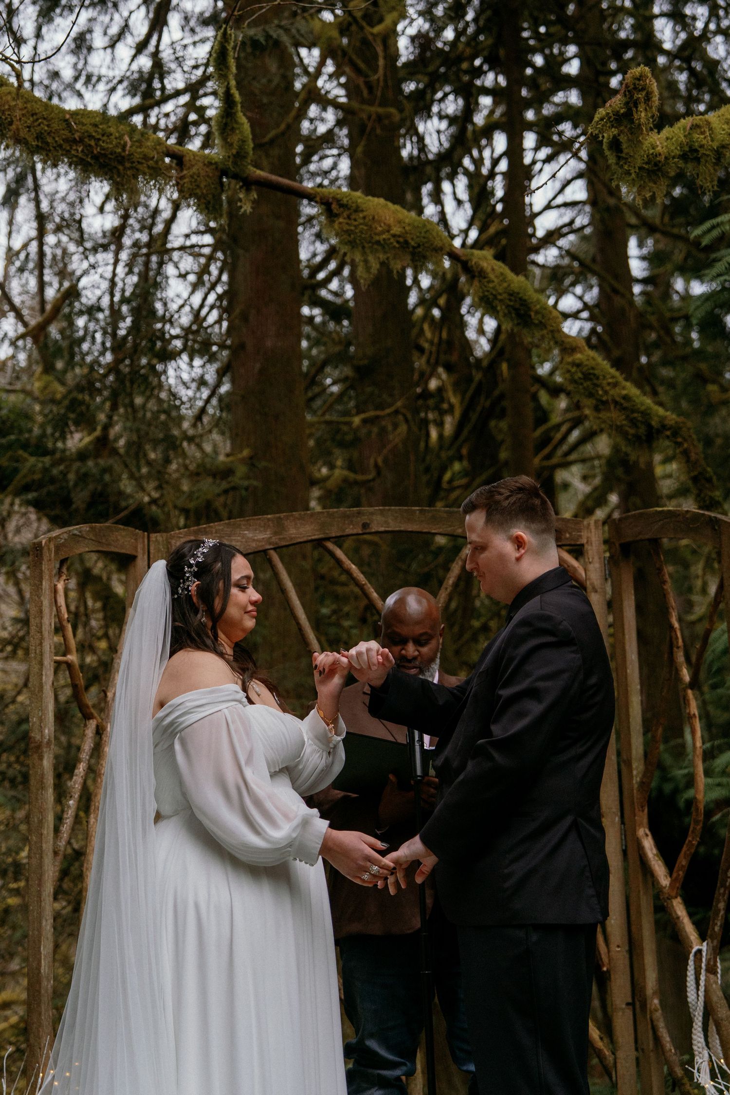 Bride and groom exchange vows at woodland wedding altar with officiant performing hand-fasting ritual.