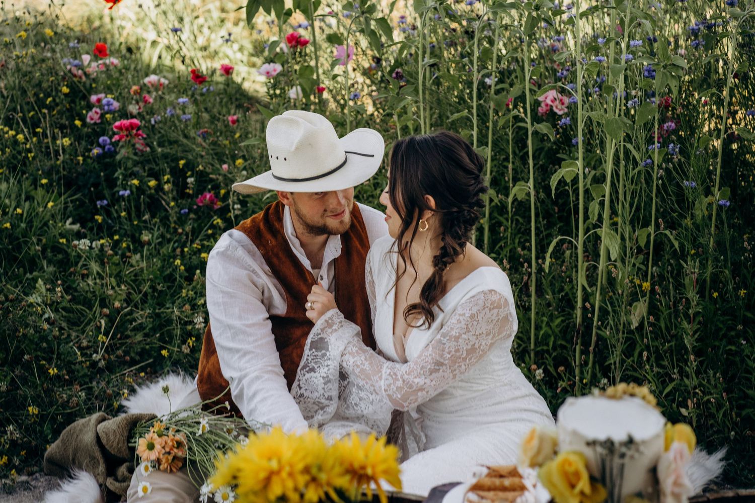 Bride and groom share a tender moment surrounded by wildflowers at a boho rustic outdoor wedding picnic.