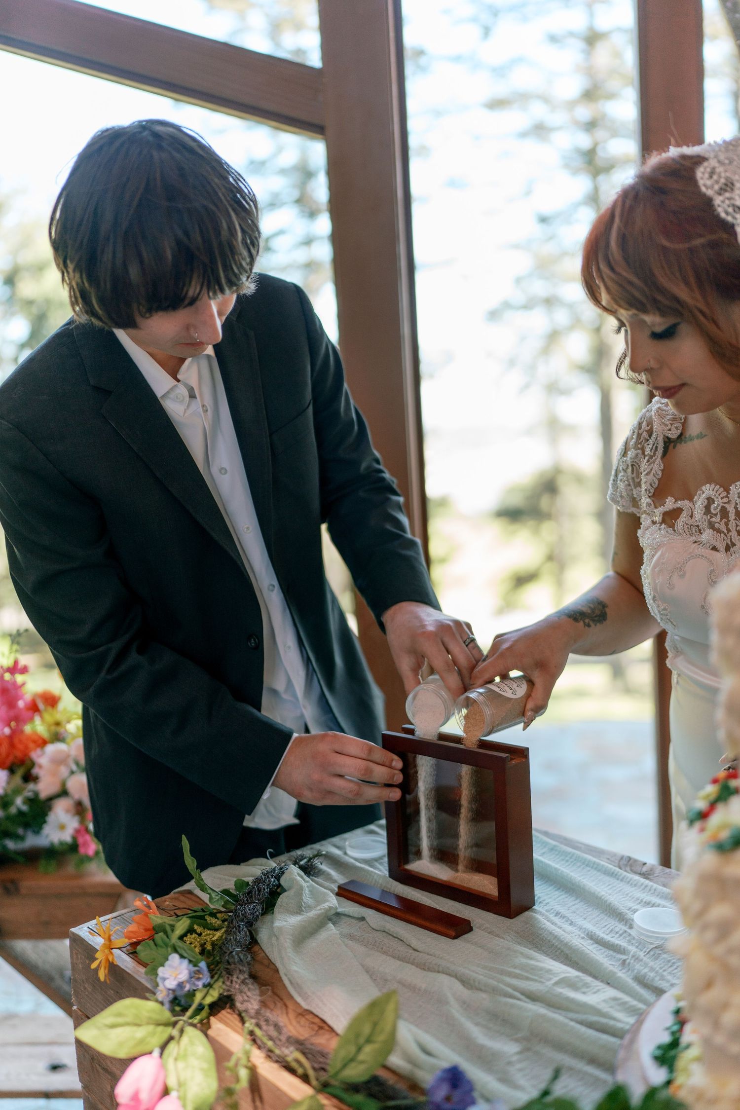 Bride and groom performing a sand unity ceremony at a decorated altar with flowers.