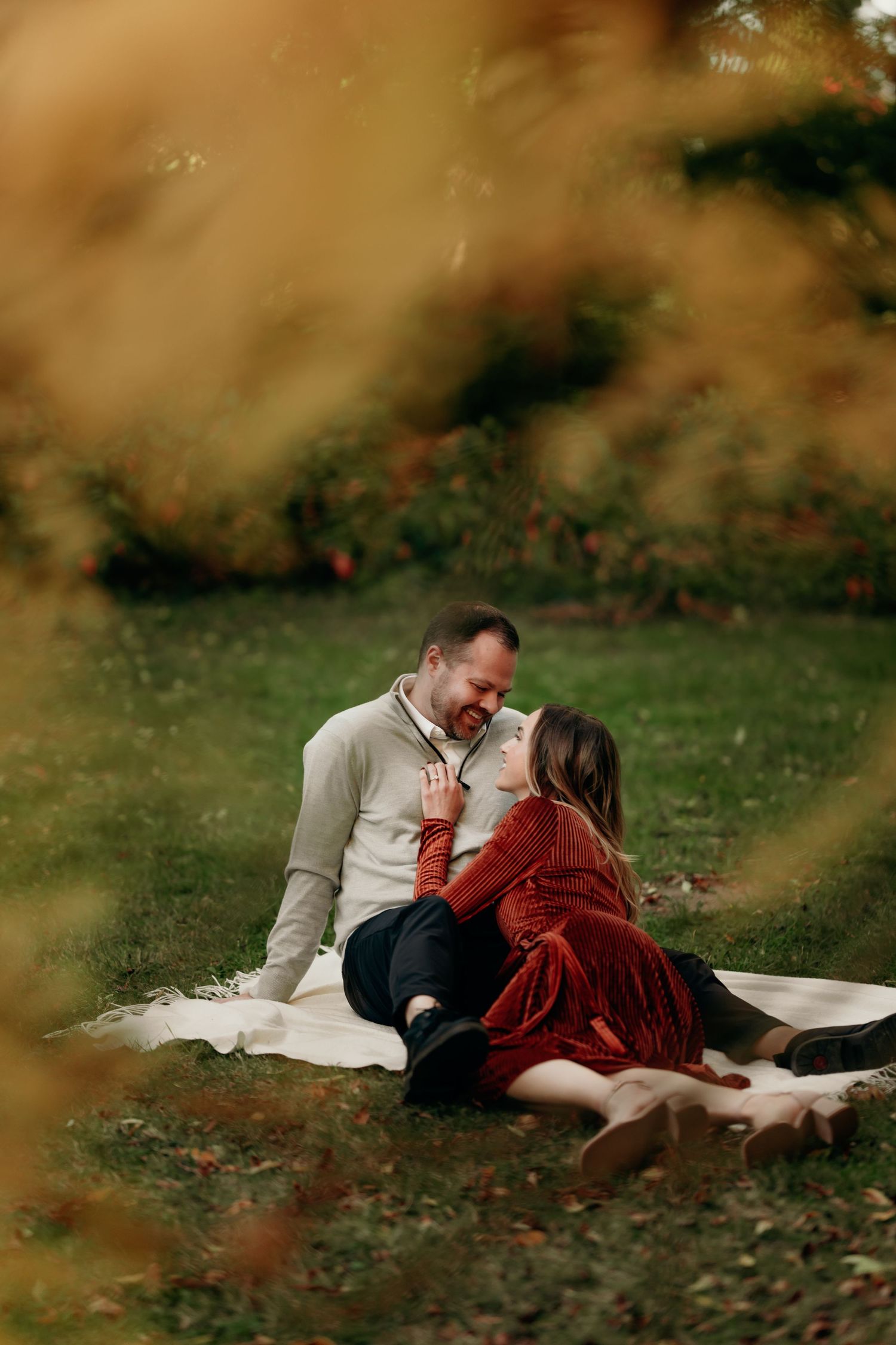 Couple sitting on a blanket in autumn park, smiling and leaning in for a kiss.