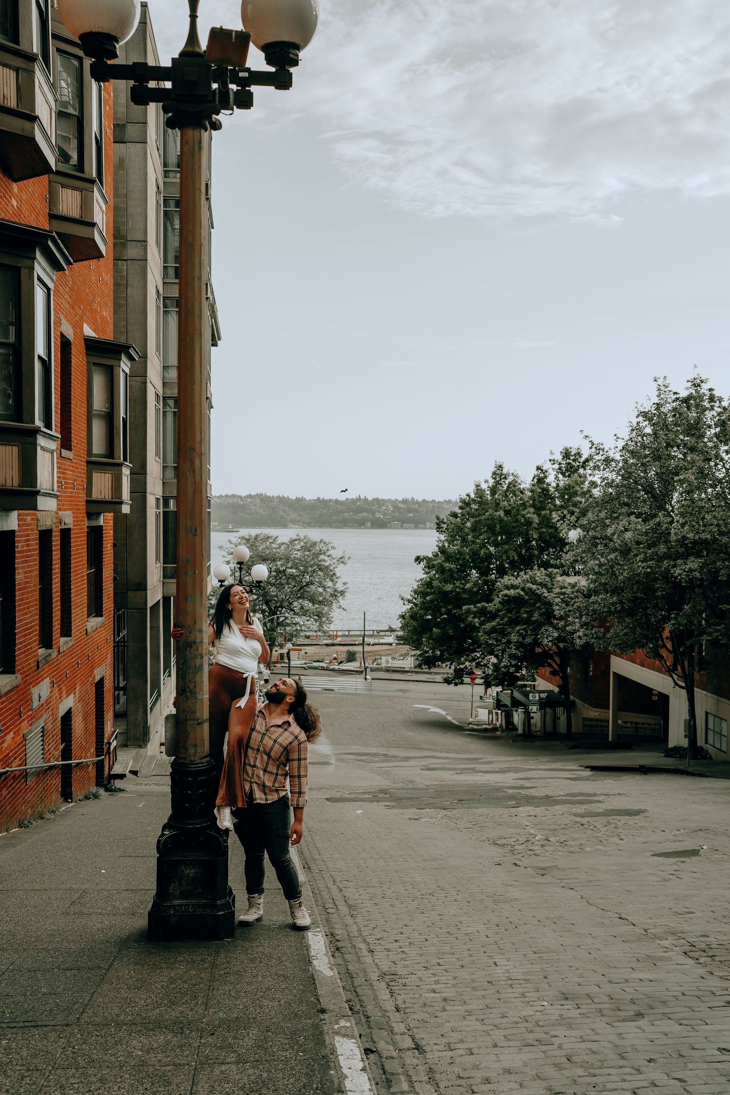 Couple standing by a lamppost on a cobblestone street with a waterfront view in Seattle.